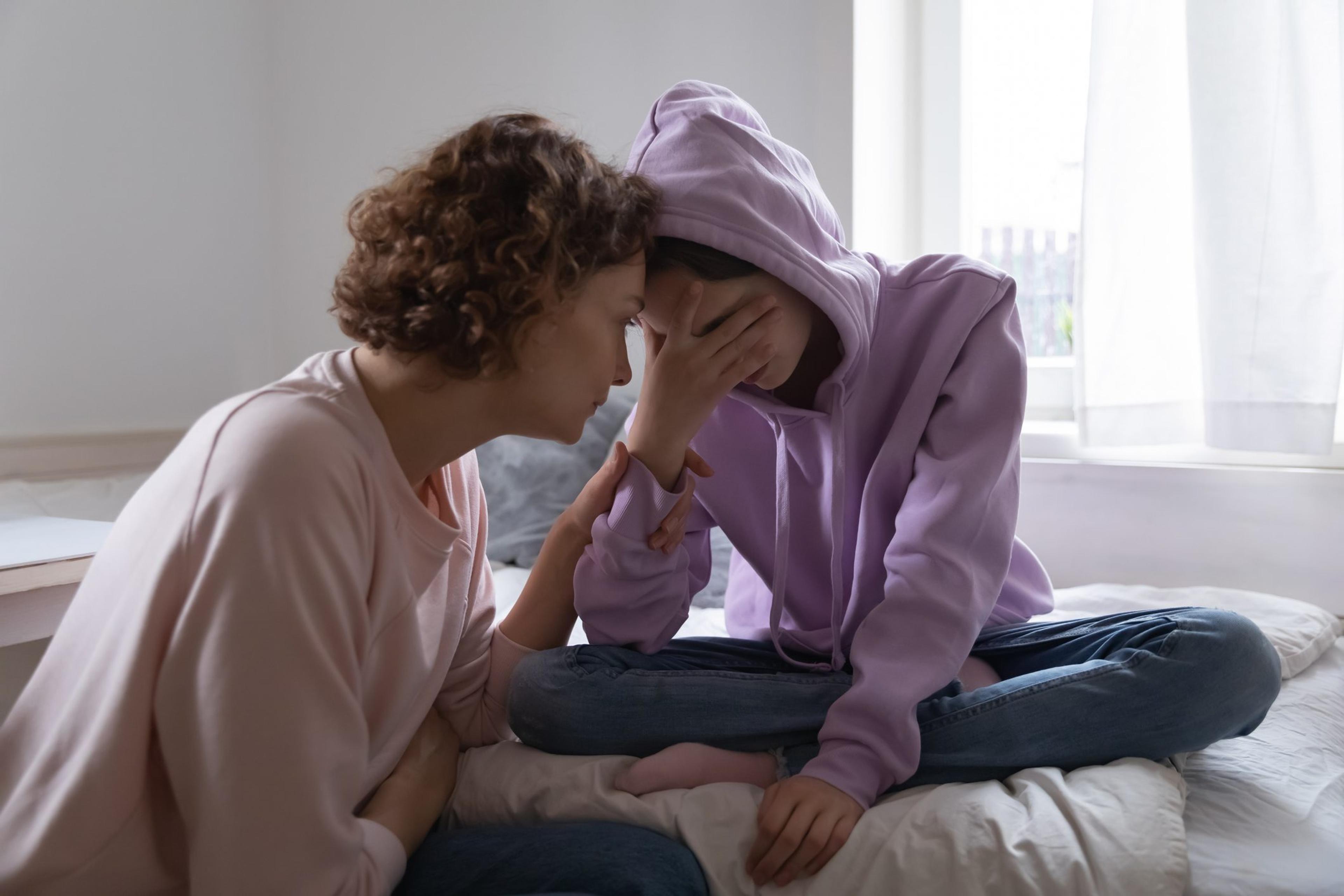 Worried mom comforting depressed teen daughter crying at home