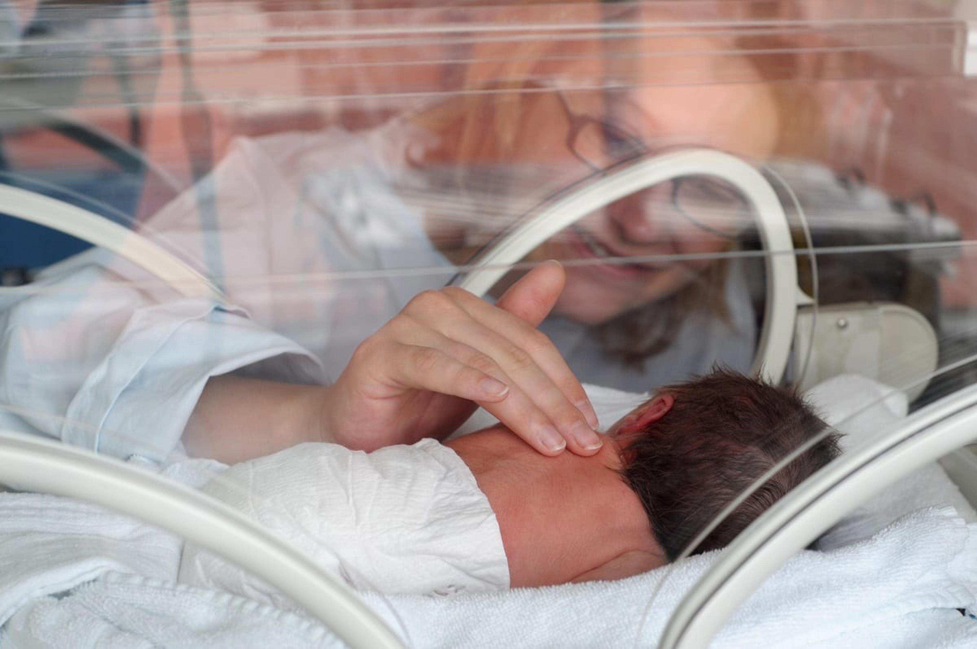 Woman comforts newborn baby in incubator