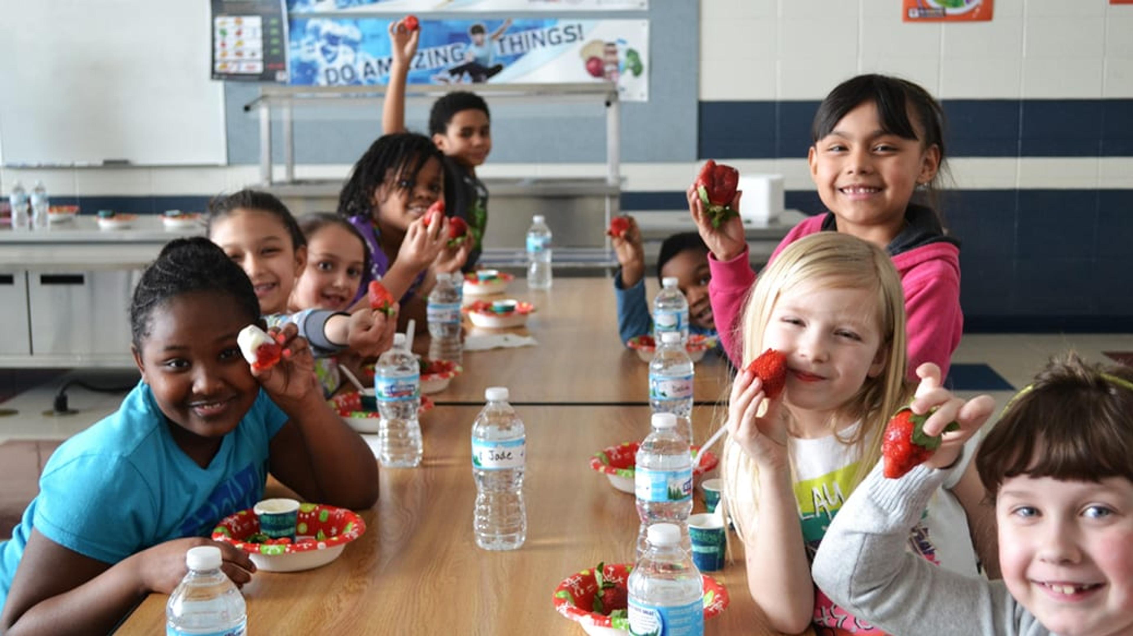 Elementary students smiling gathered at a lunch table with healthy foods