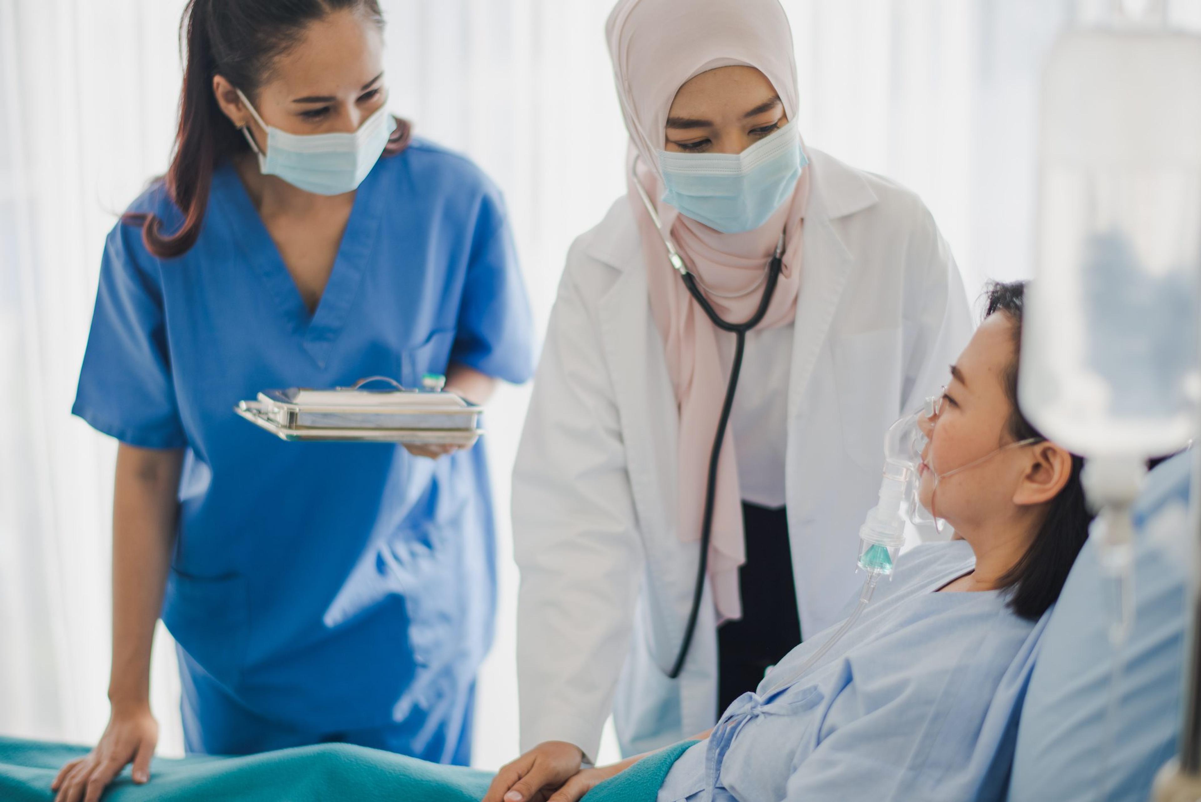 Young Asian woman Muslim doctor and nurse giving advice discussion and check up to elderly patient sitting in bed at hospital which smiling and felling happy. Medicine and health care safe concept.