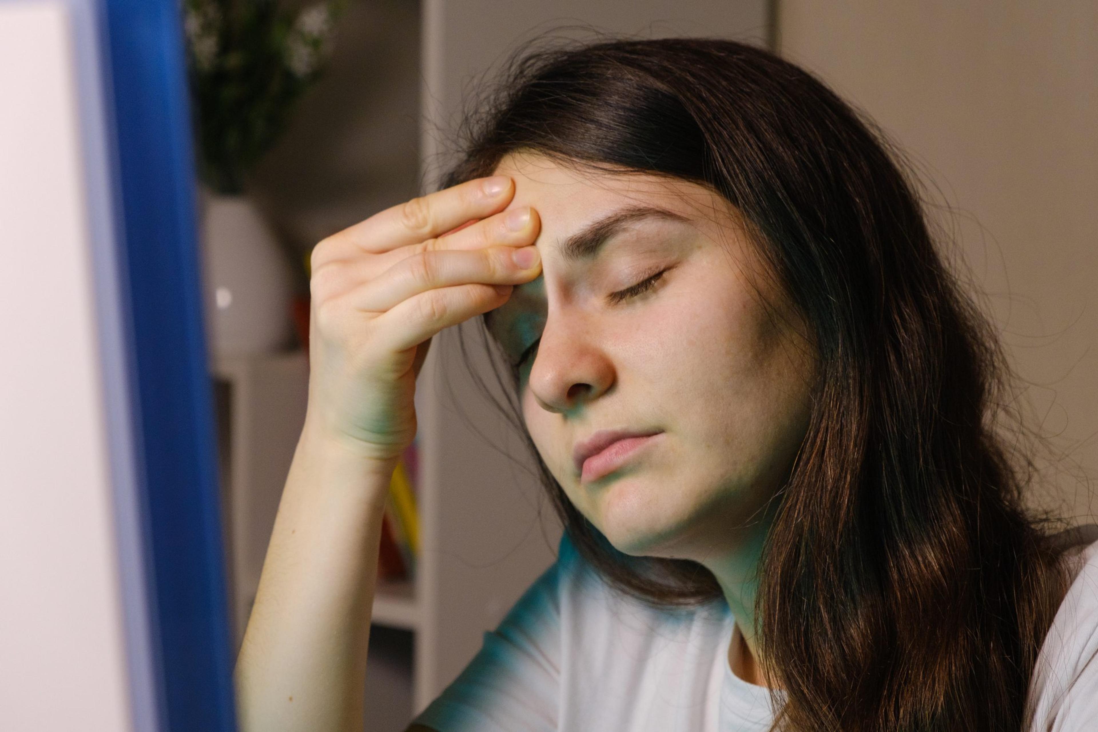 A tired woman holds her hand by the forehead, sitting in front of a computer screen