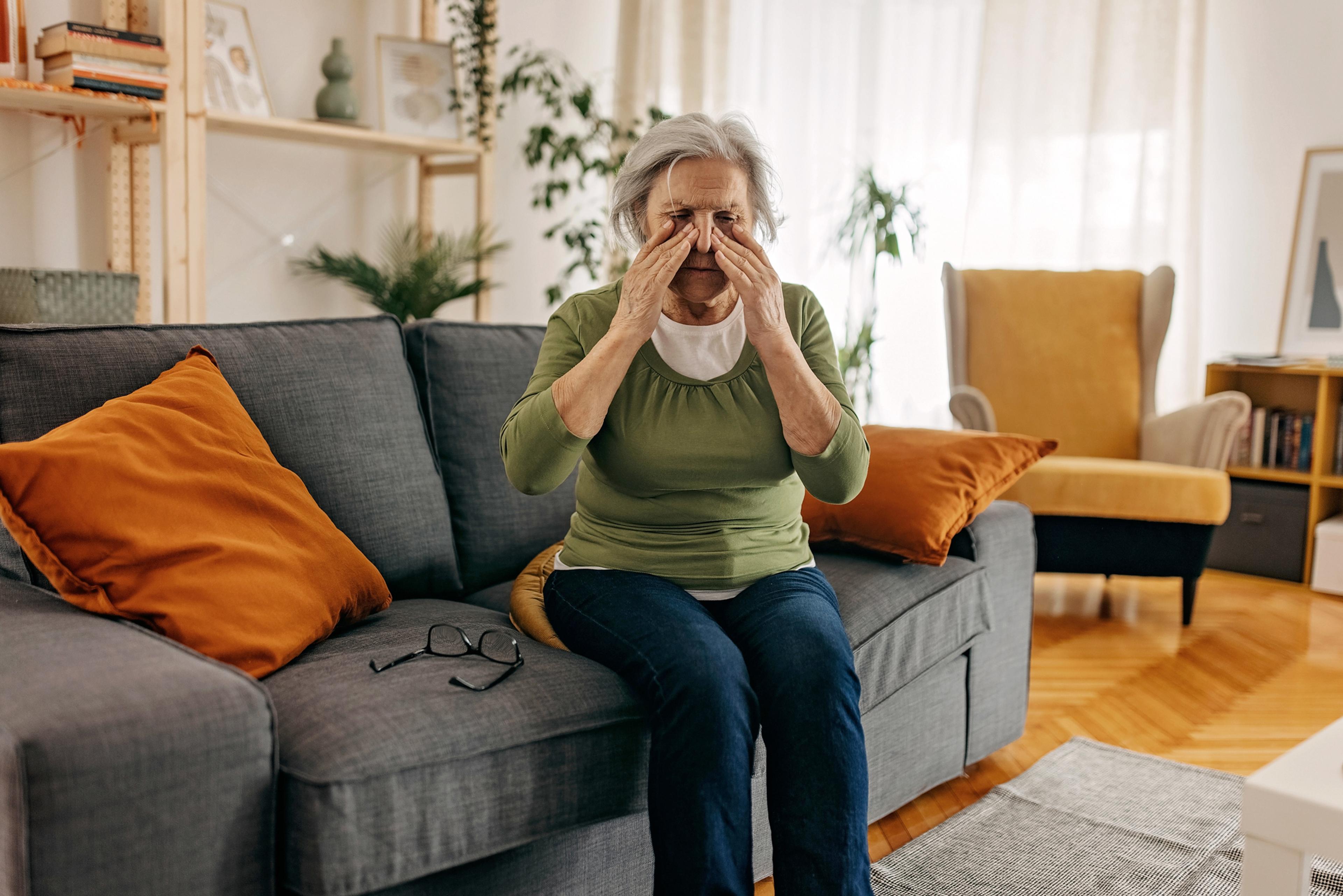 Senior woman having headache and sinusitis, sitting in her living room