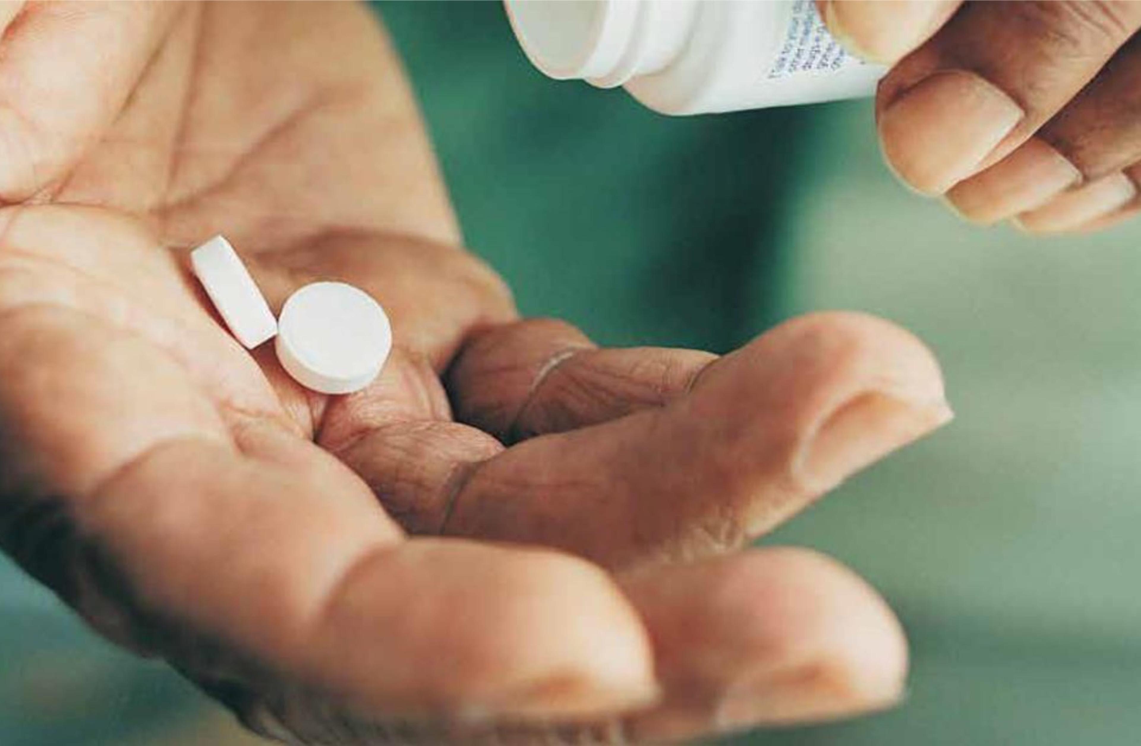 A hand holding two pills from a prescription bottle