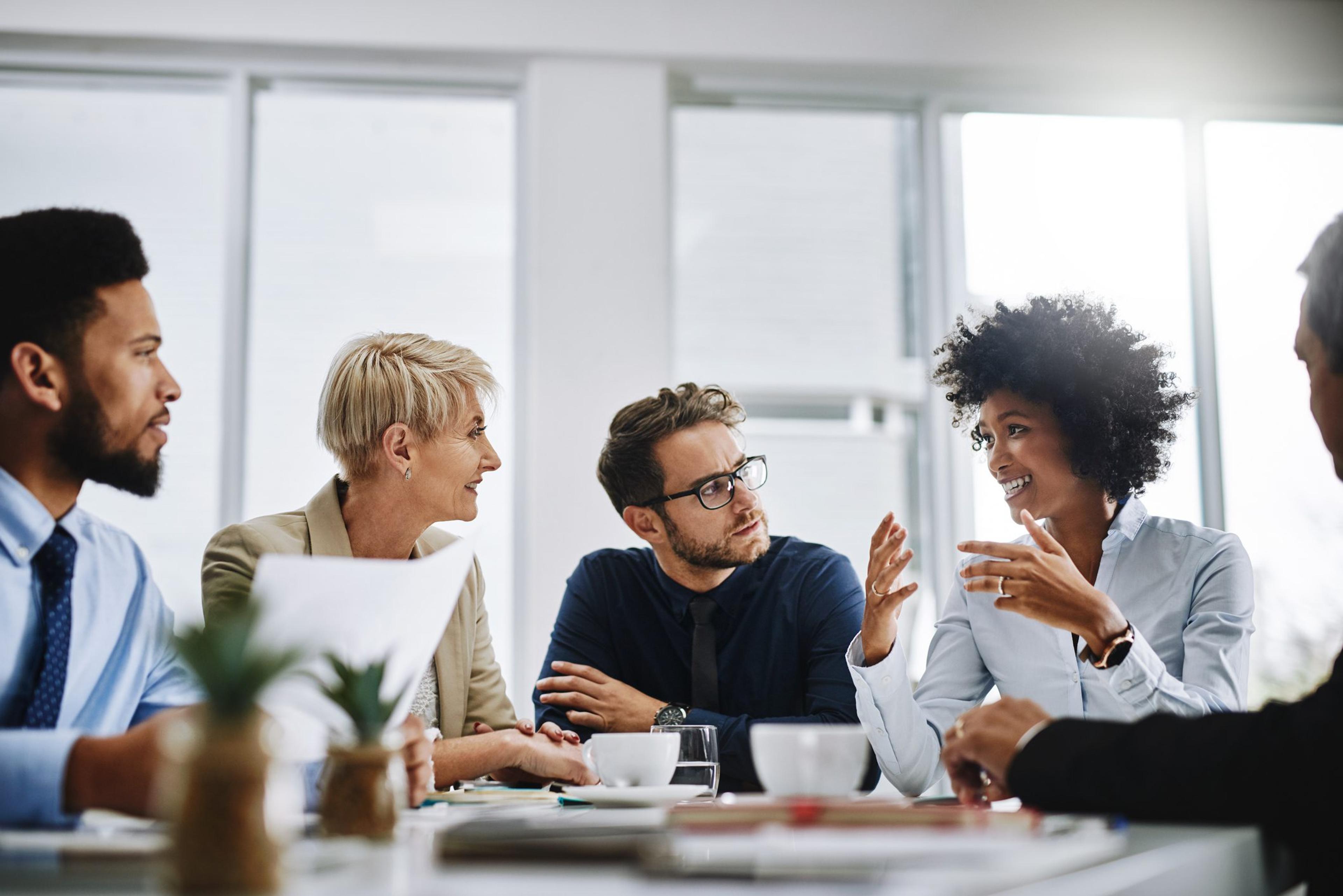 A group of diverse colleagues sits around a table discussing business.