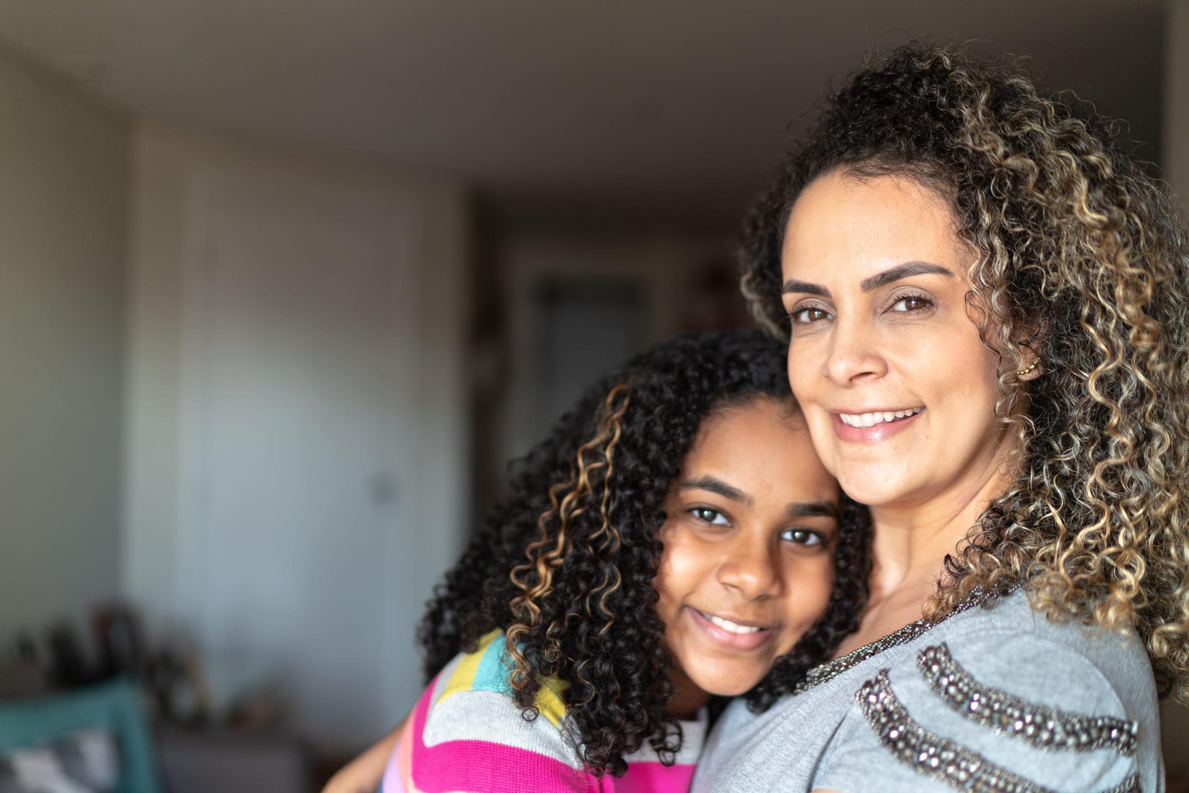 A woman and young girl embrace and look at the camera as they pose for a portrait