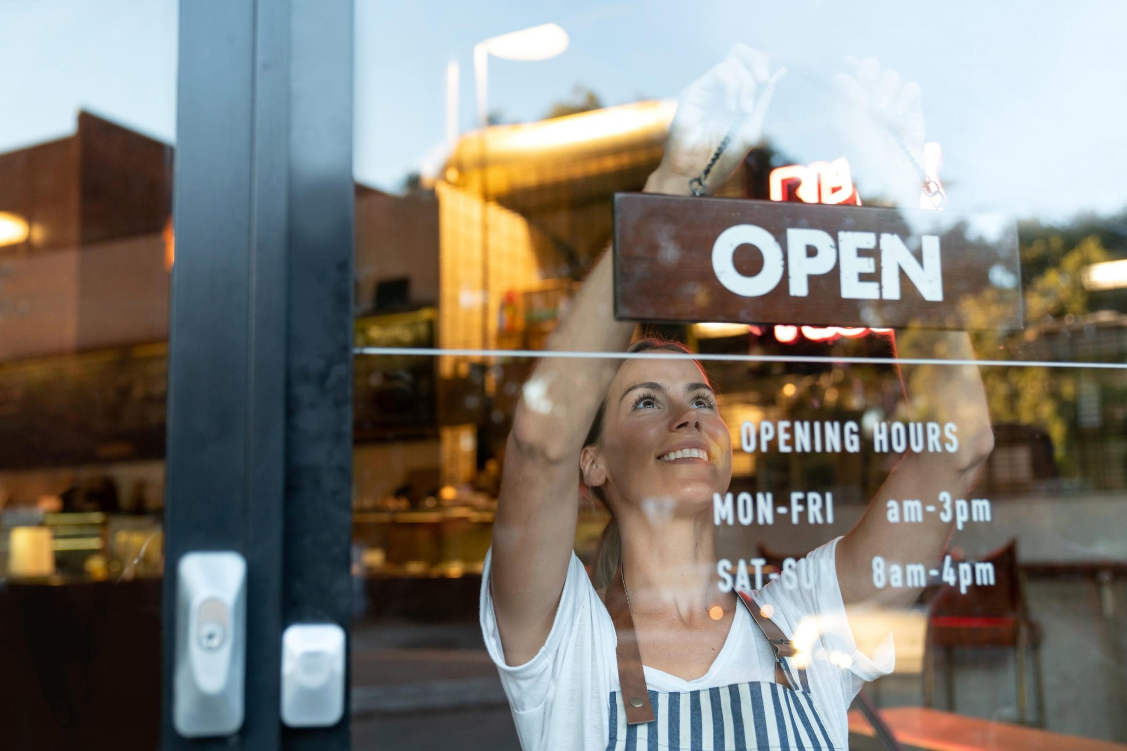 Woman turning around an "open" sign at her shop