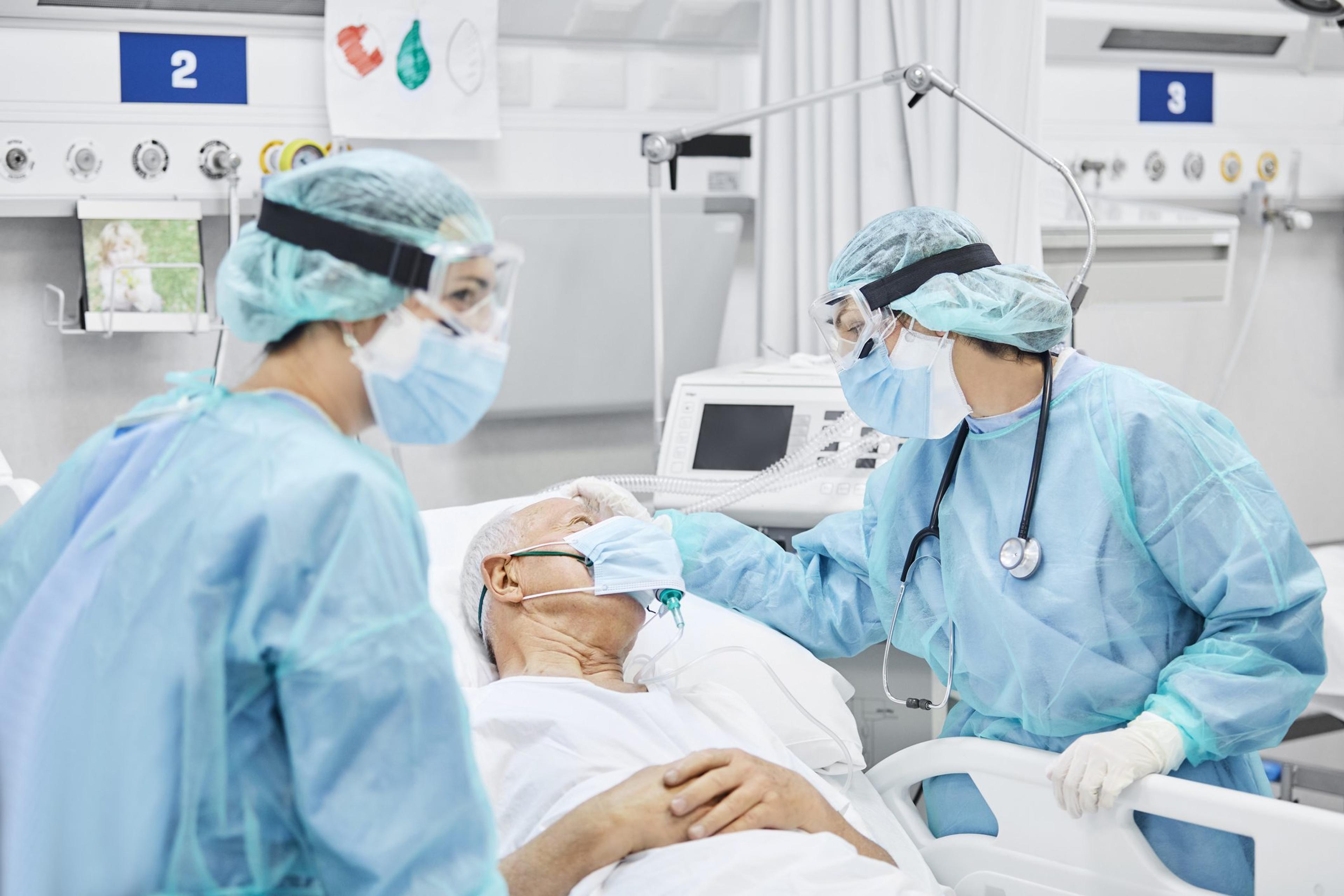 Doctors in full PPE talk with a hospital patient wearing a mask