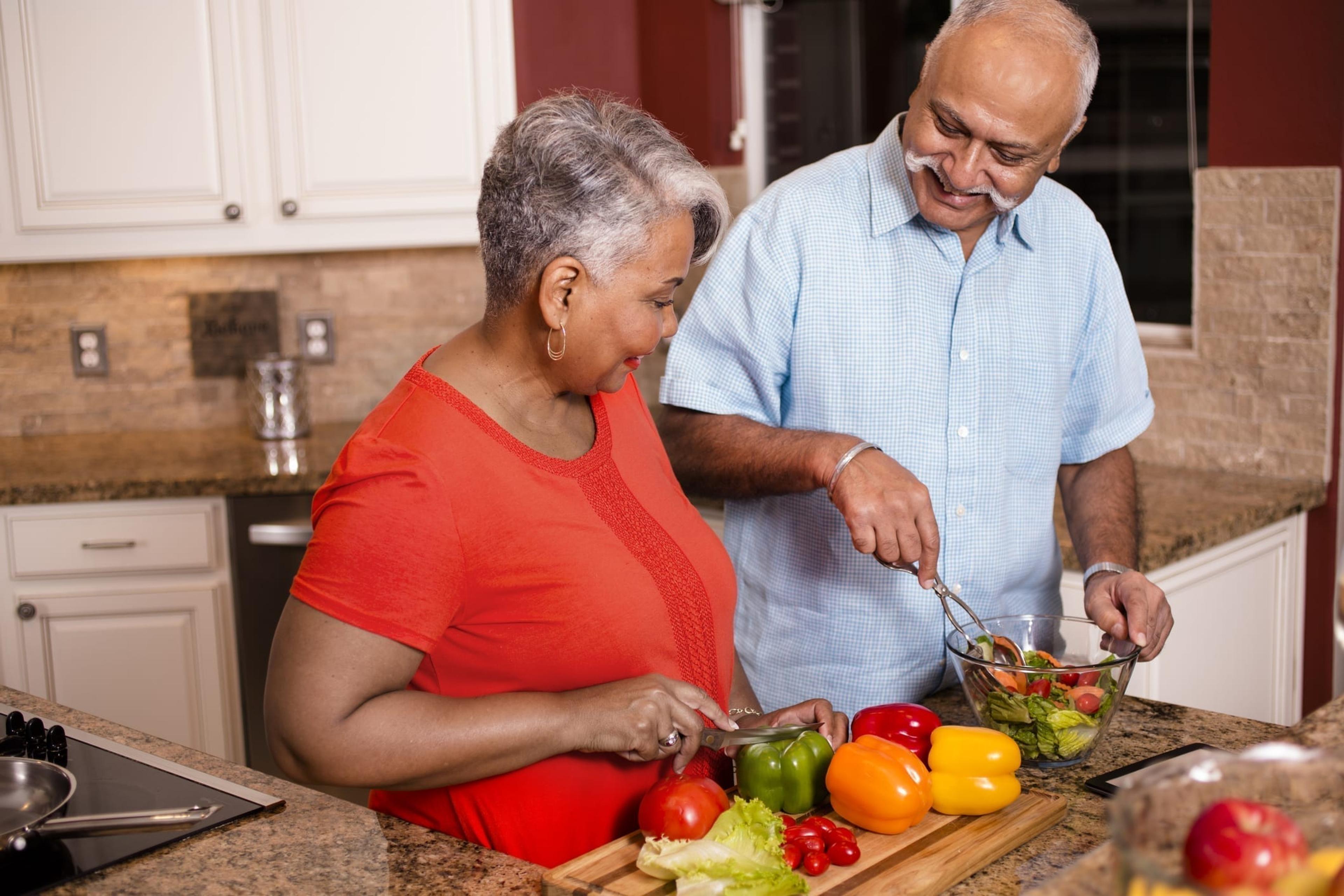 Happy senior adult couple cooking together in home kitchen.