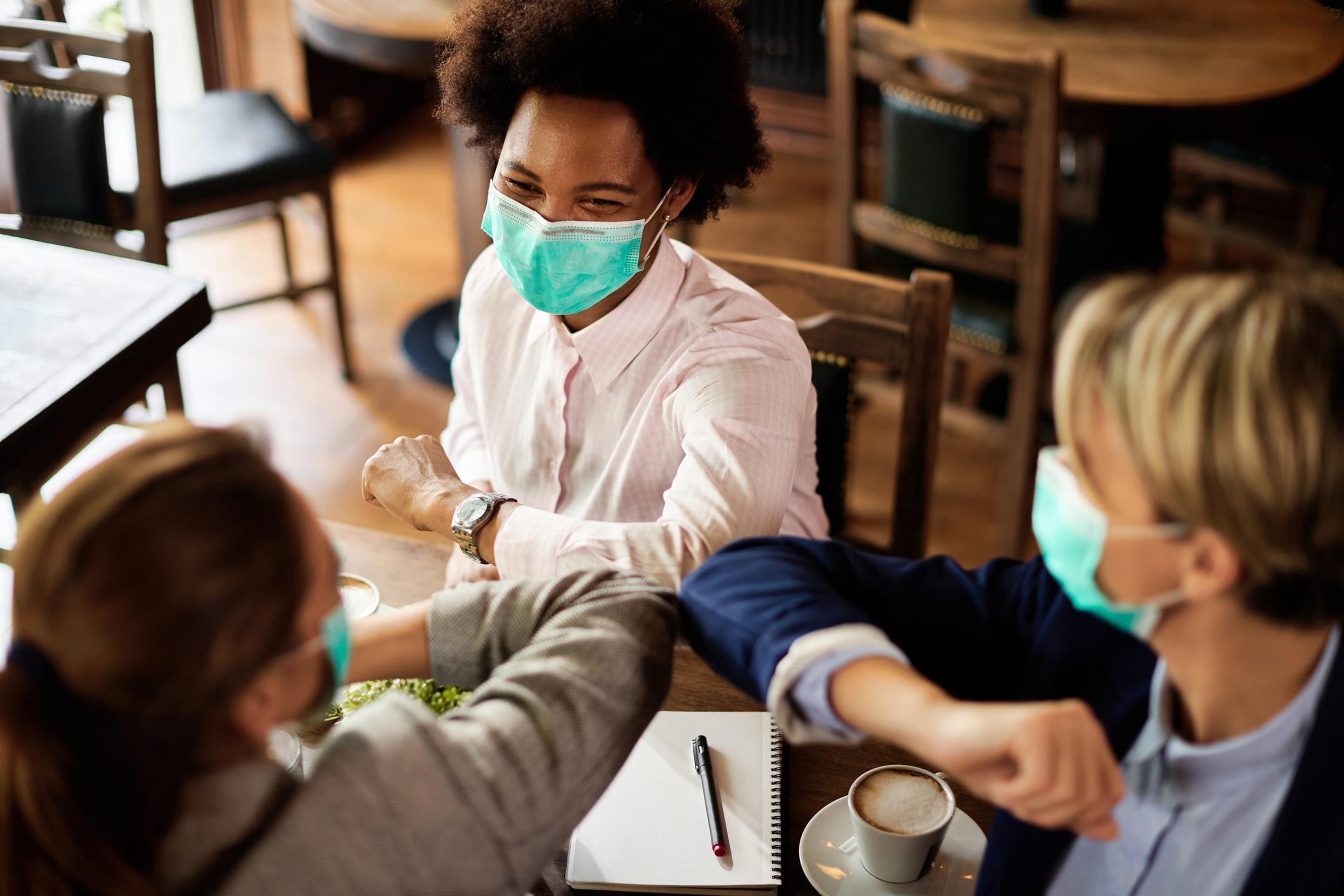 Female colleagues wearing masks bump elbows after a meeting