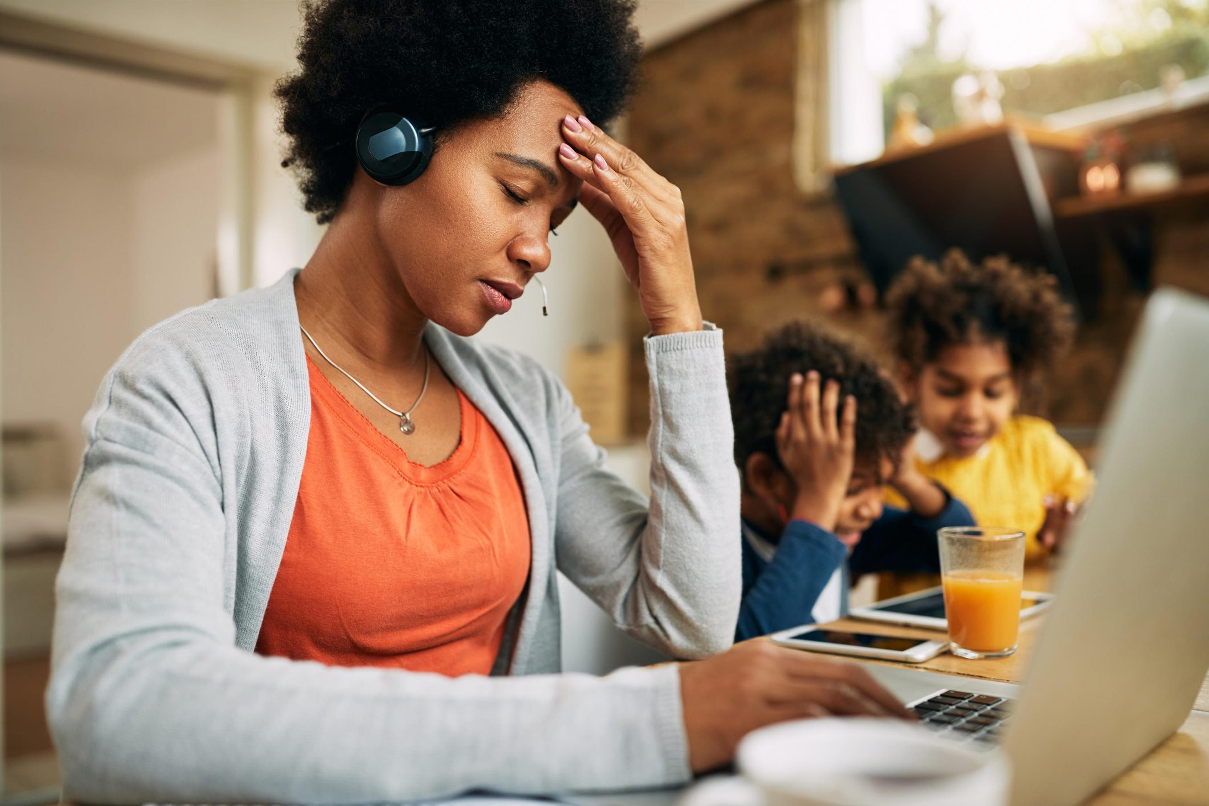 Stressed woman leans on her hand while sitting at the table with her children