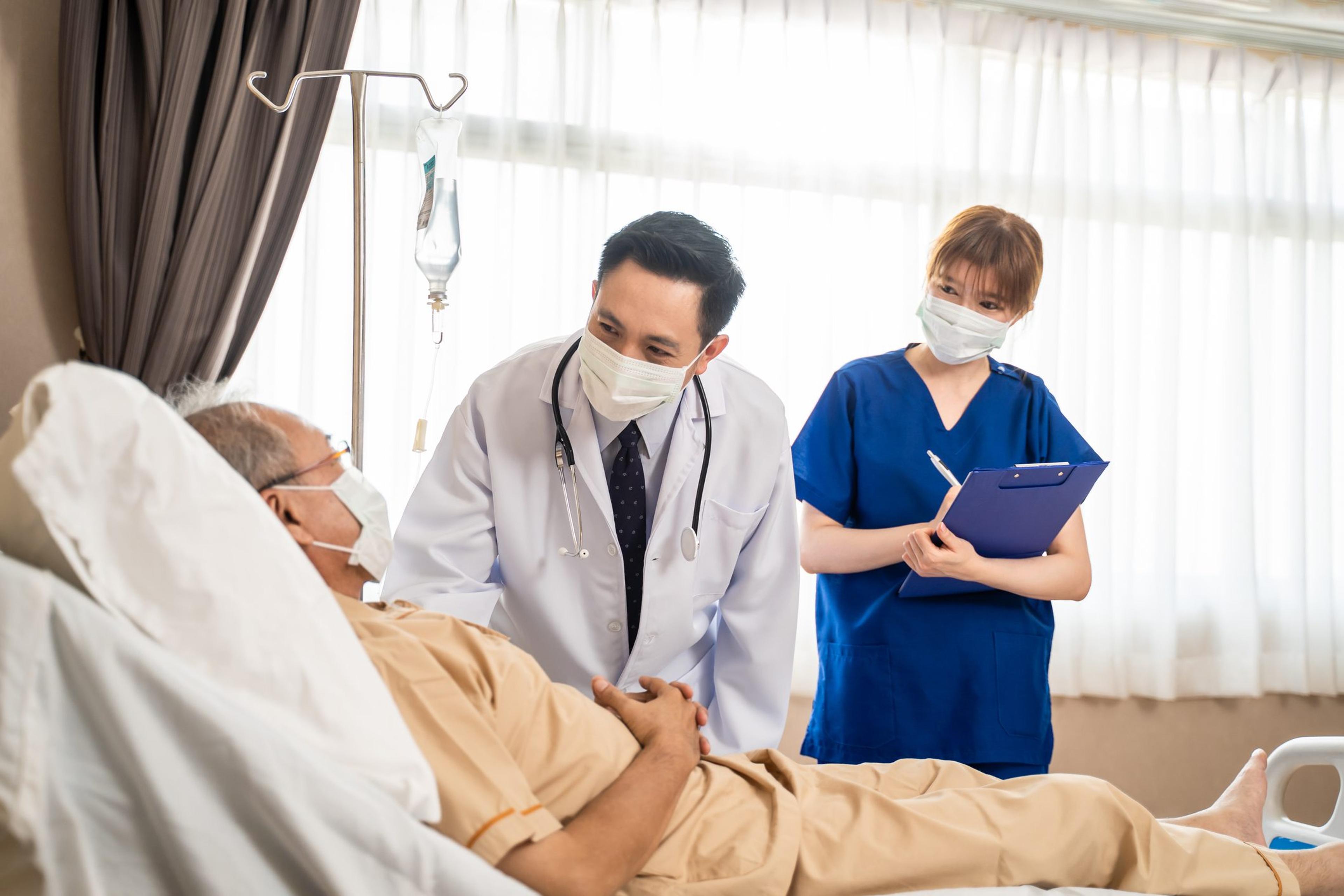 Doctor wearing a mask checks in with a patient in a hospital bed