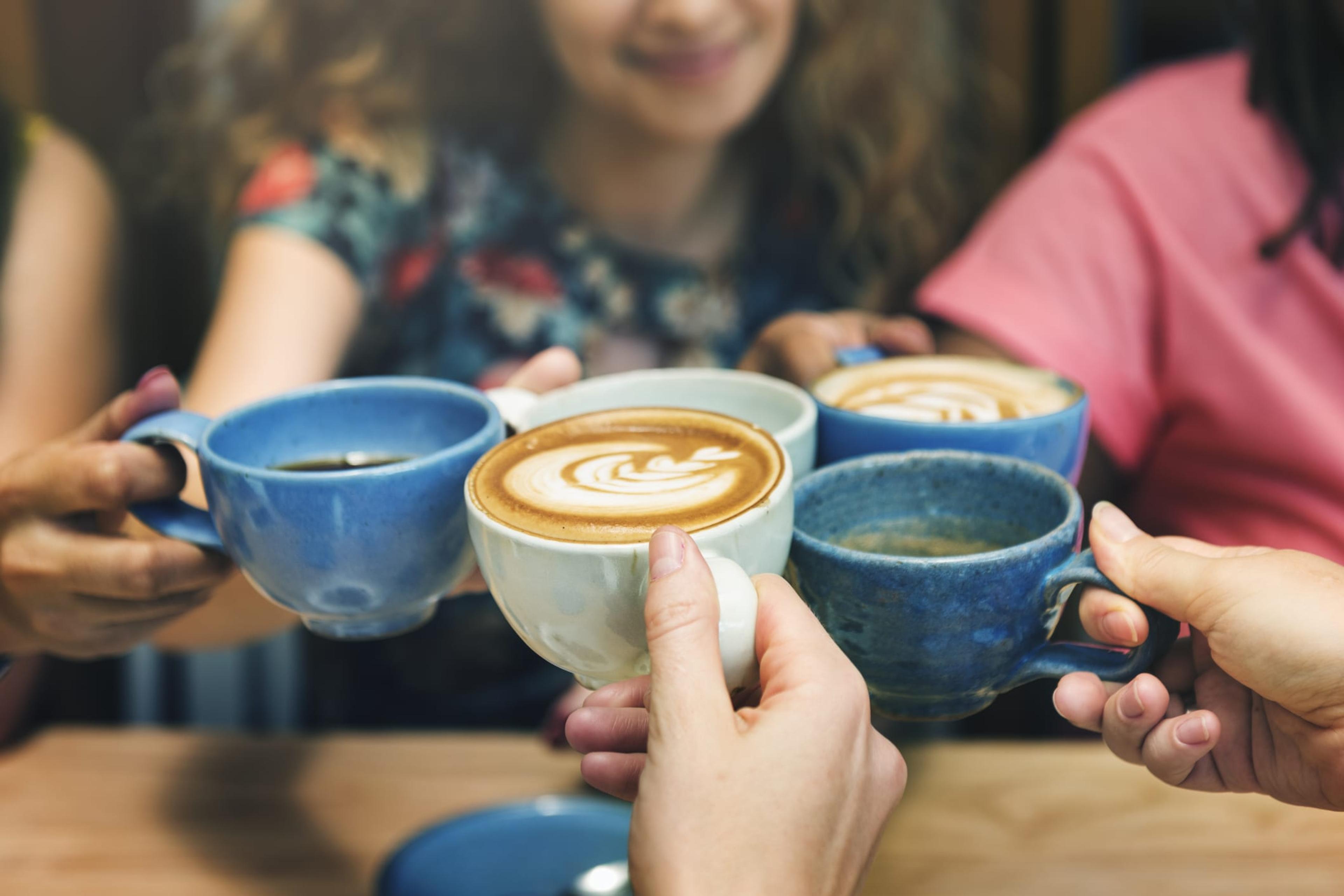 Young women toasting full coffee mugs at a coffee shop.