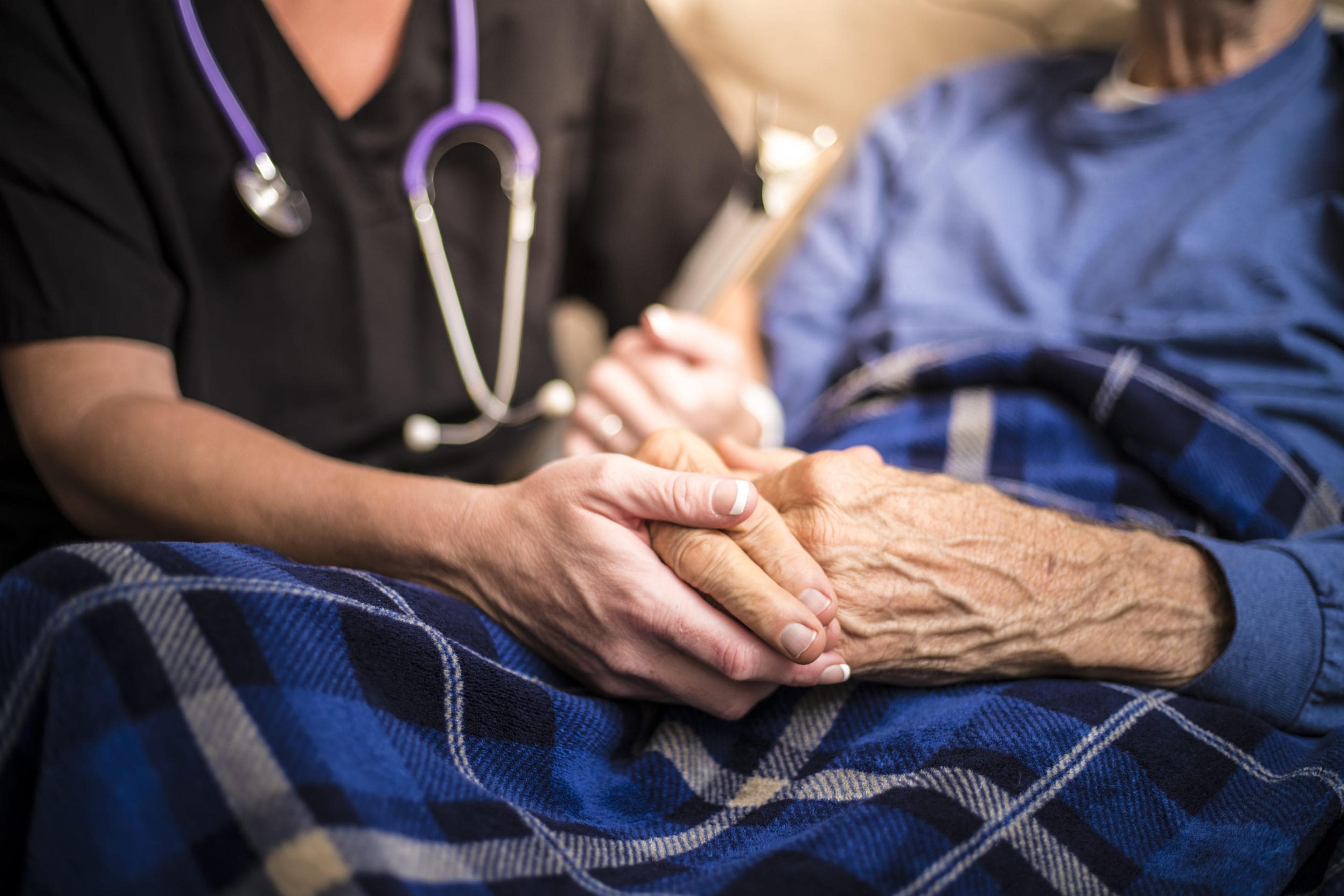 Image of a medical professional holding an elderly man's hands.