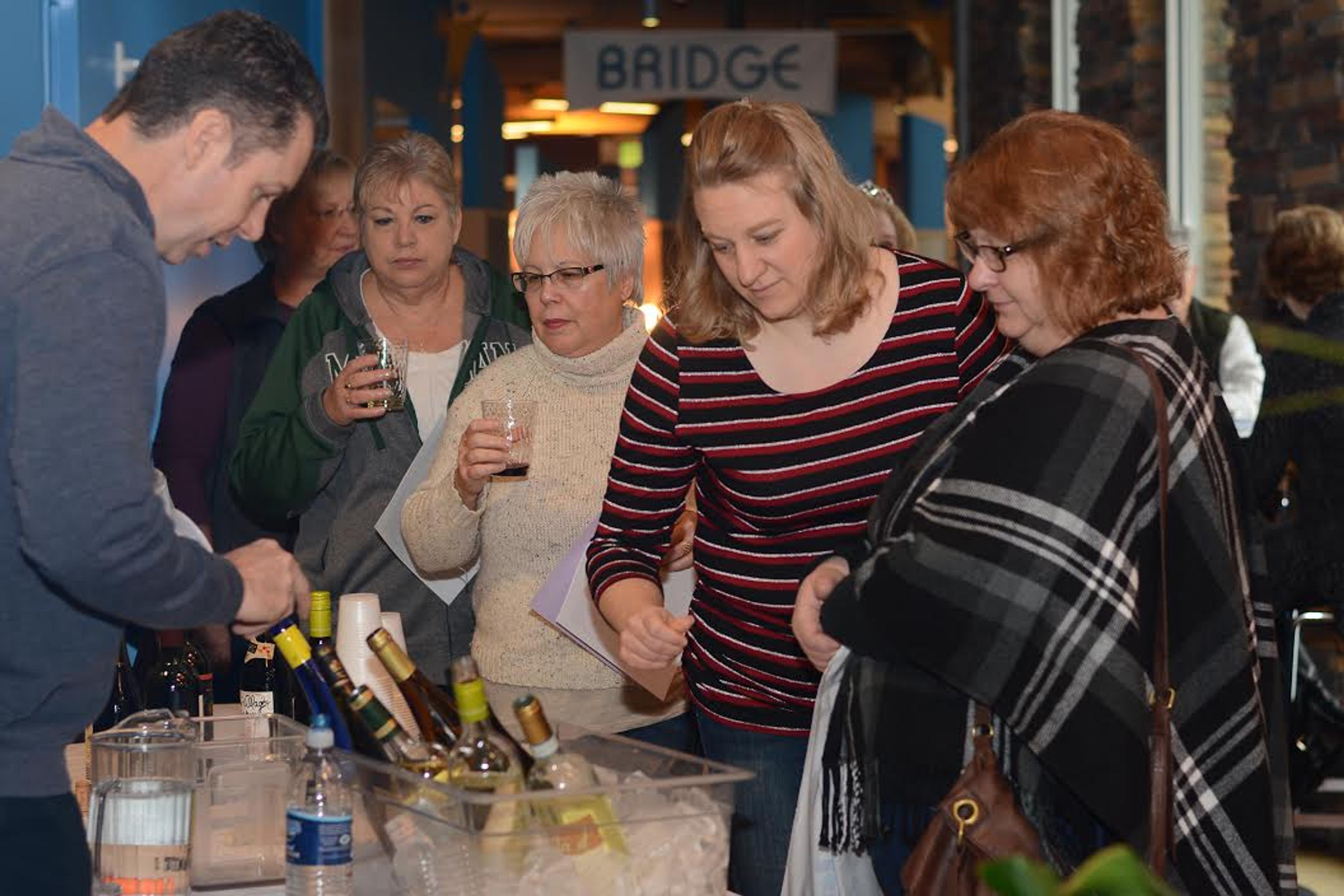 four women standing at a table where wine is being served.