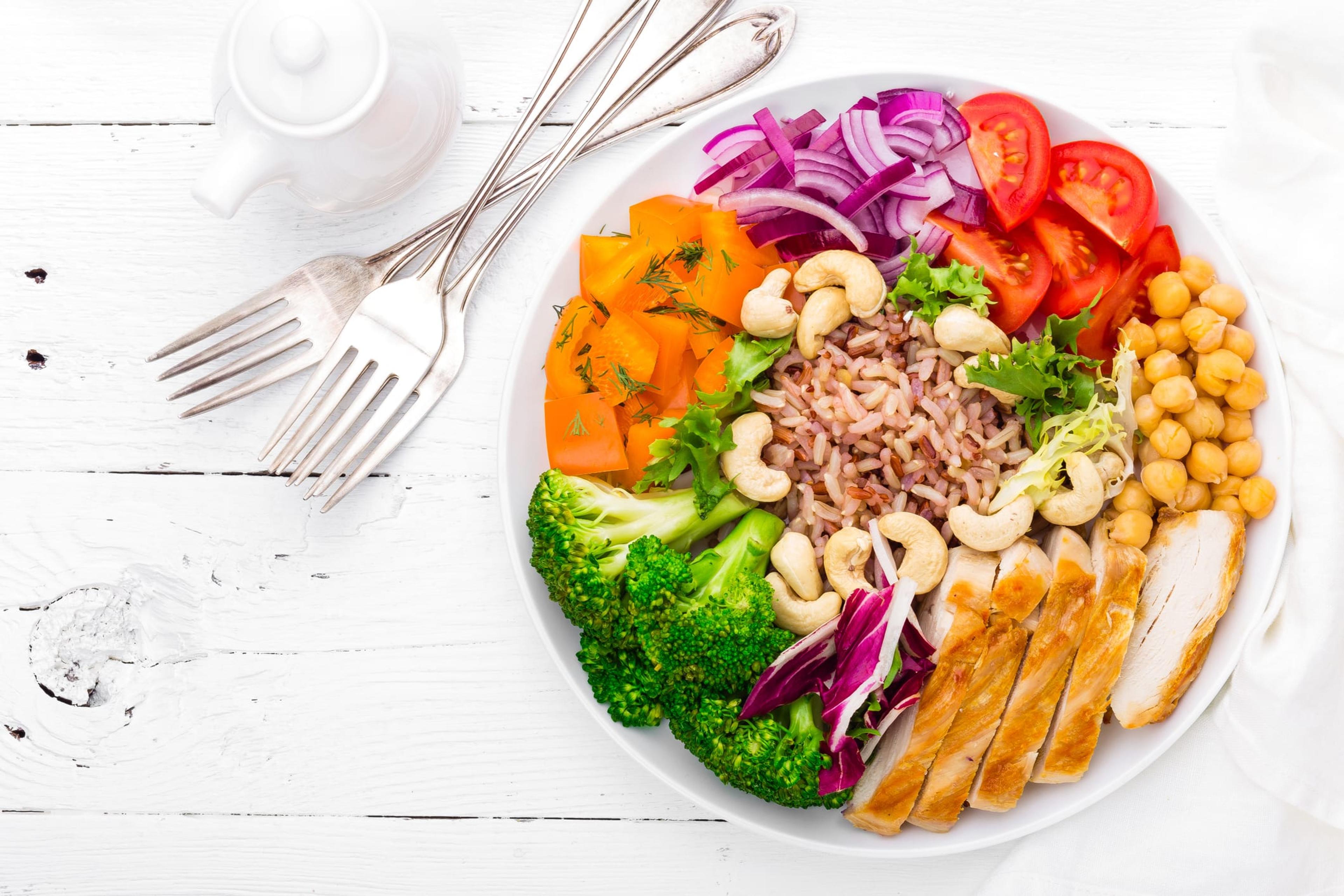 Buddha bowl dish with chicken fillet, brown rice, pepper, tomato, broccoli, onion, chickpea, fresh lettuce salad, cashew and walnuts. Healthy balanced eating. Top view. White background