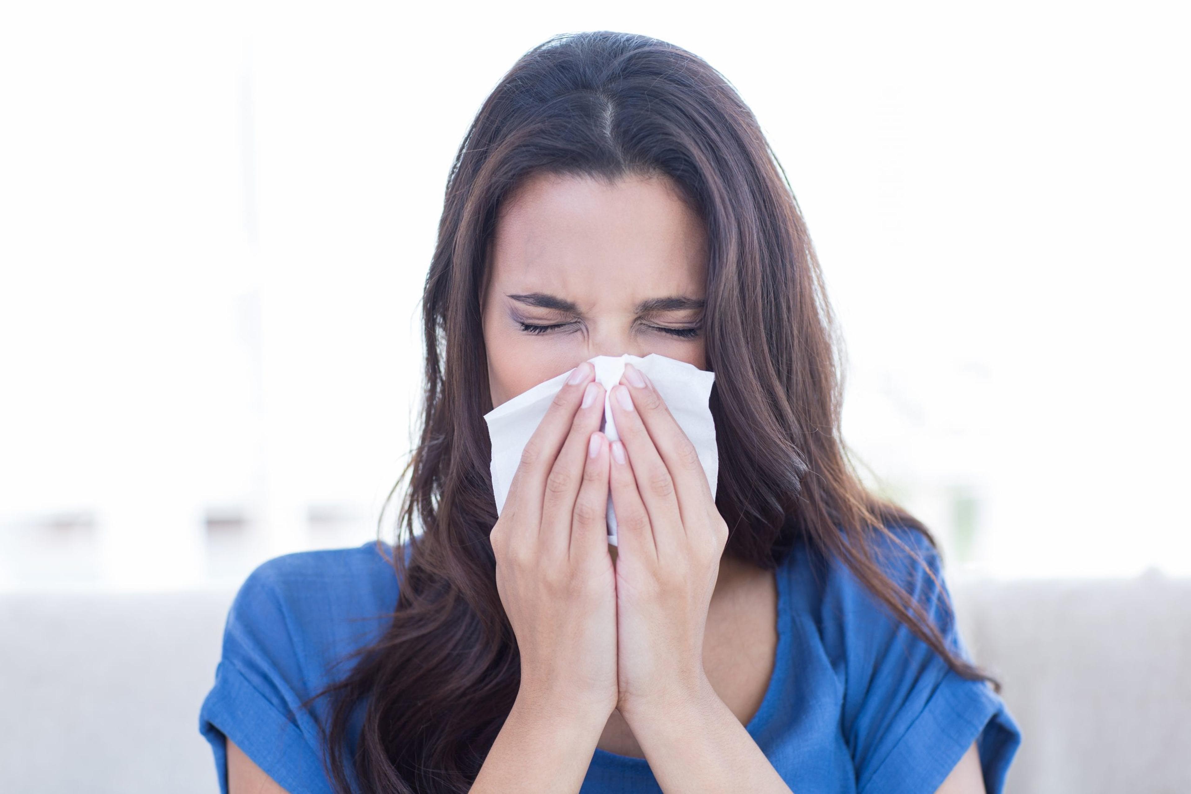 Woman sneezing into a tissue.