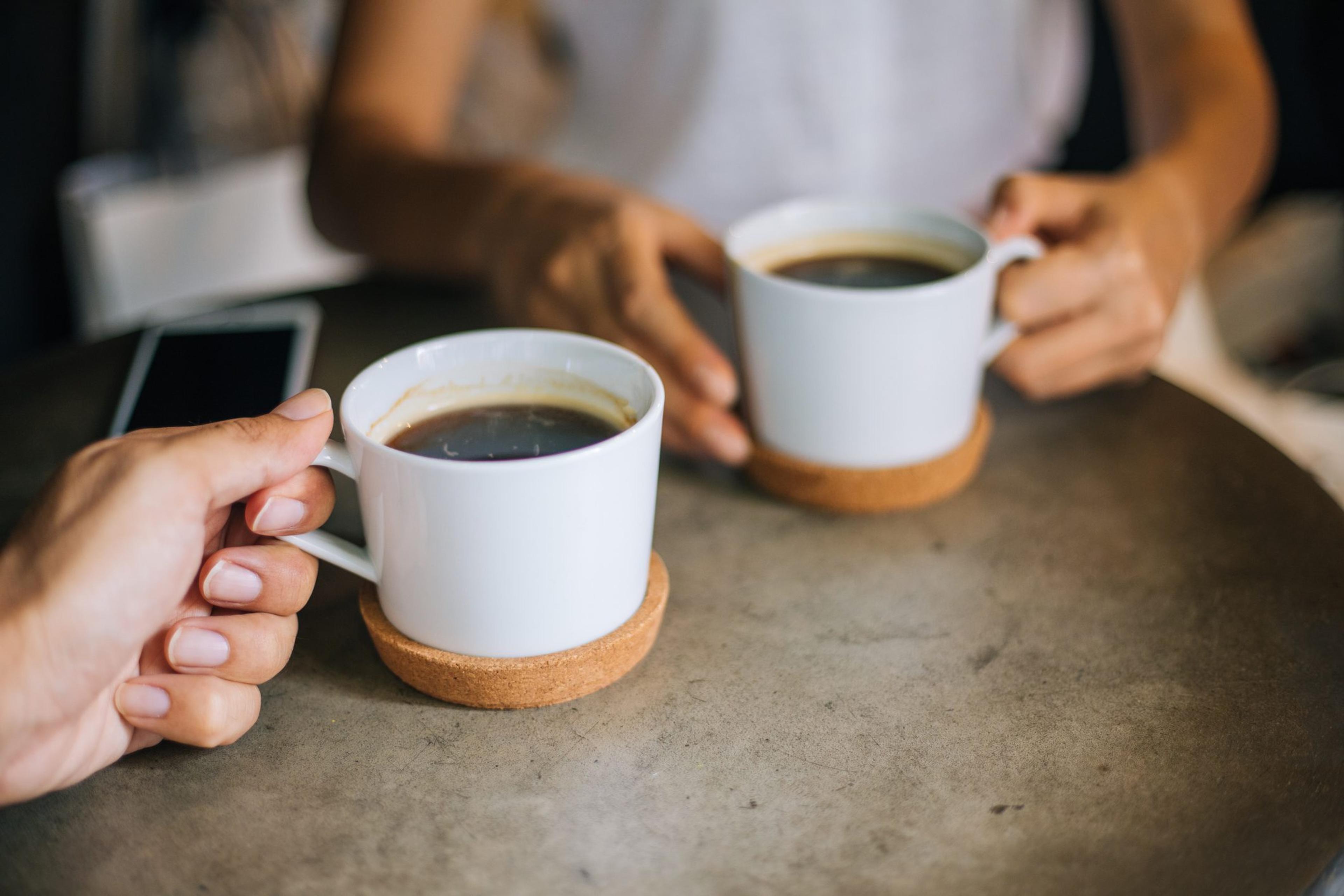 Close up of two people holding coffee cups at the table