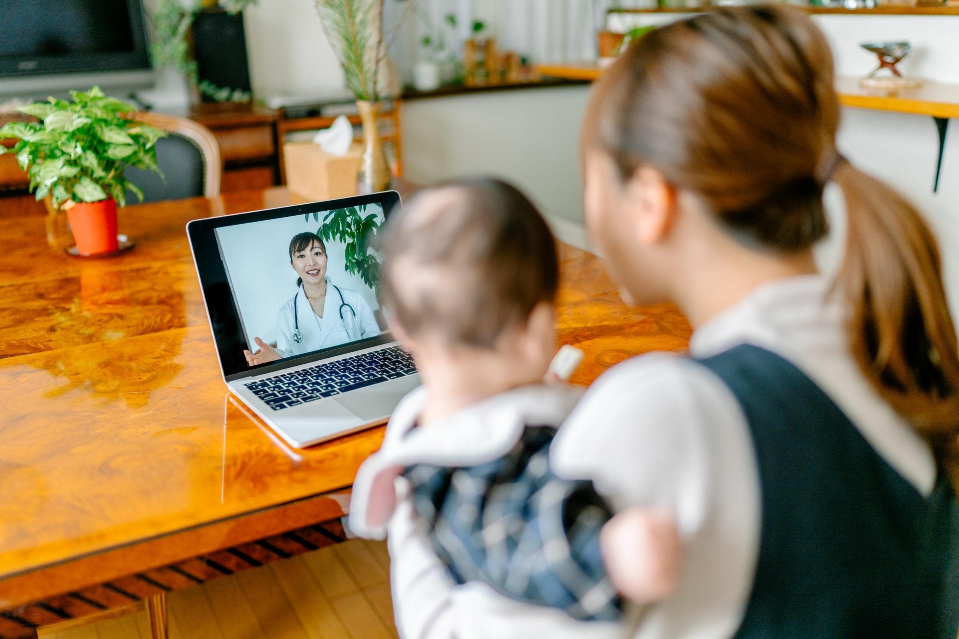 Mom with baby on her lap talking to a doctor on her laptop