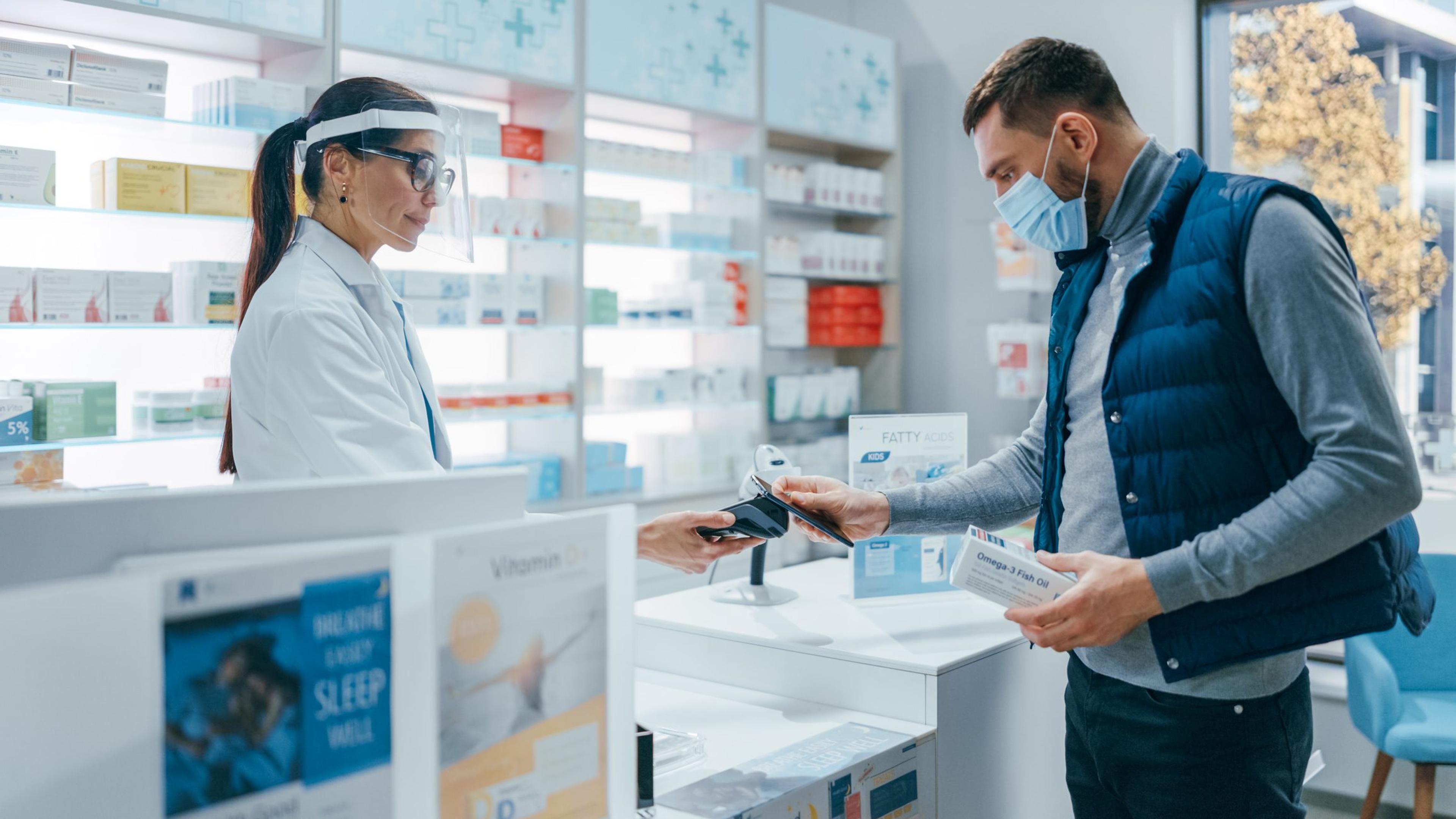 Man wearing a mask hands his credit card to a pharmacist