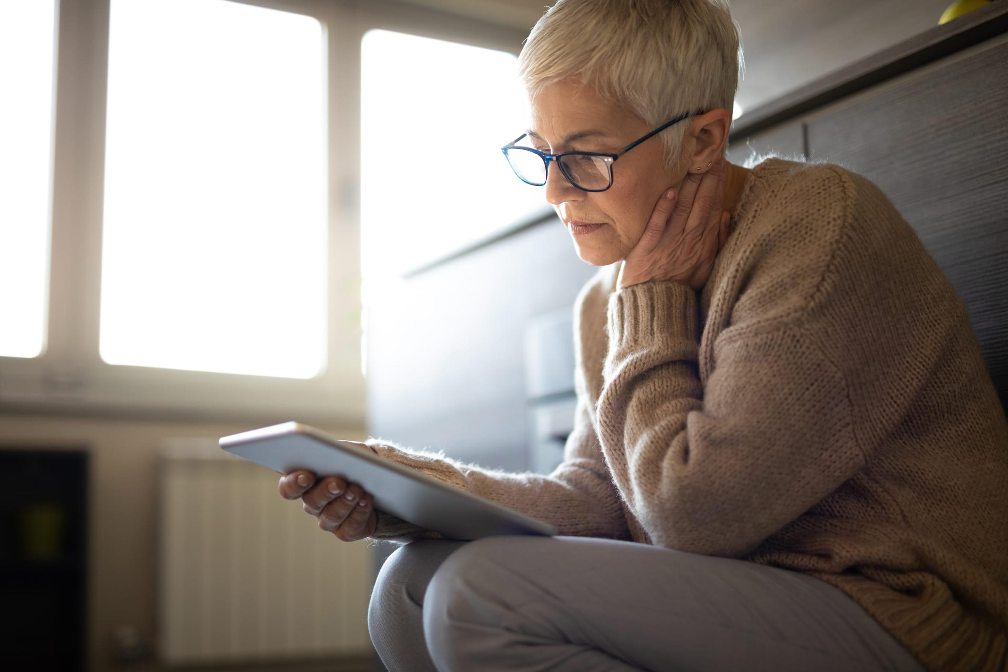 Worried senior woman reading an e-mail on tablet