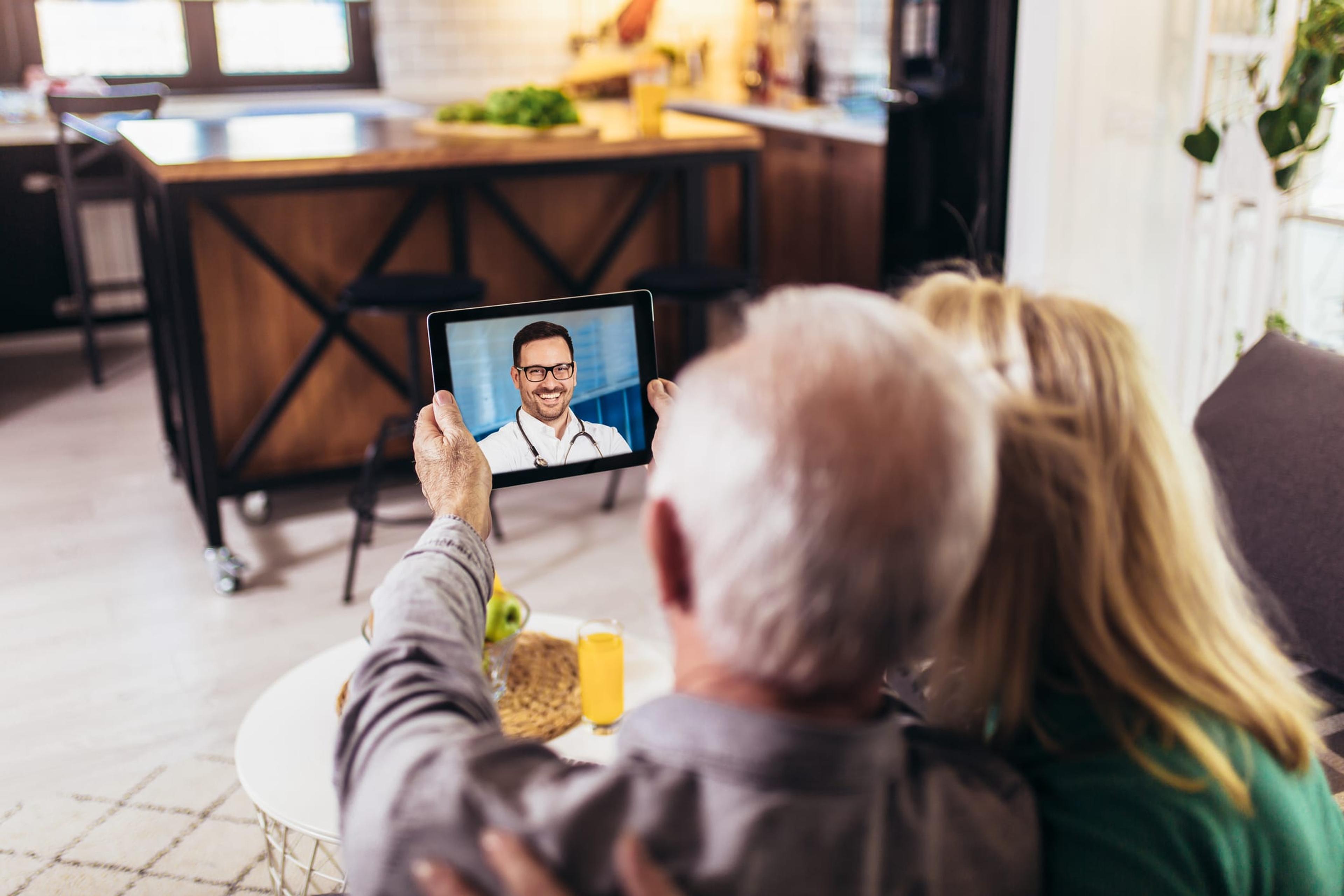 A senior couple hosts a telehealth meeting on a tablet with a physician.