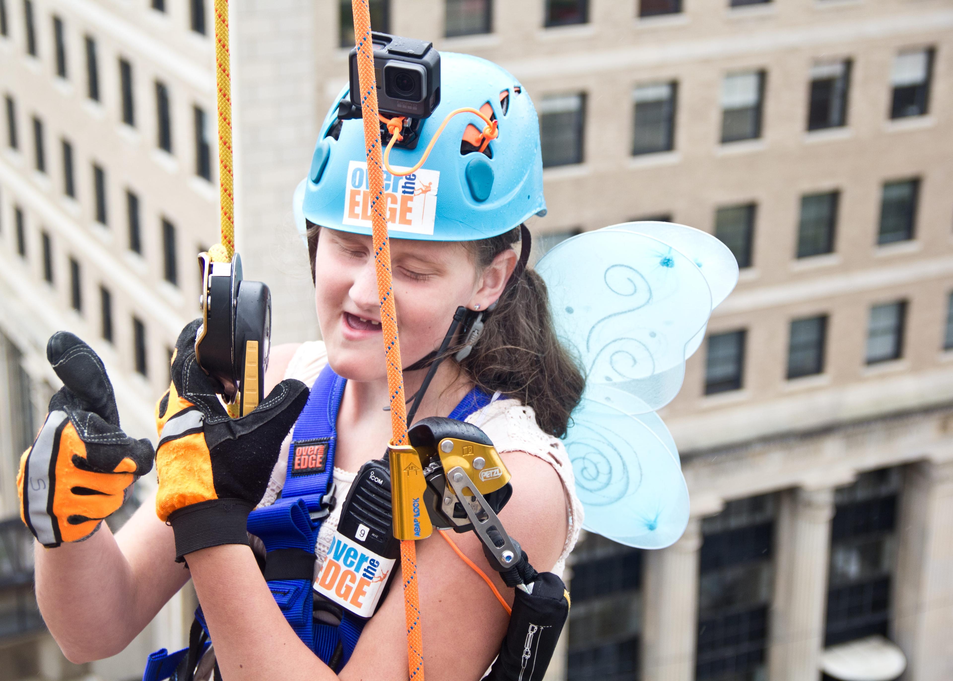 Image of Riley Letterman wearing a helmet, harness and angel wings as she rappels down the Durant Building in Flint.
