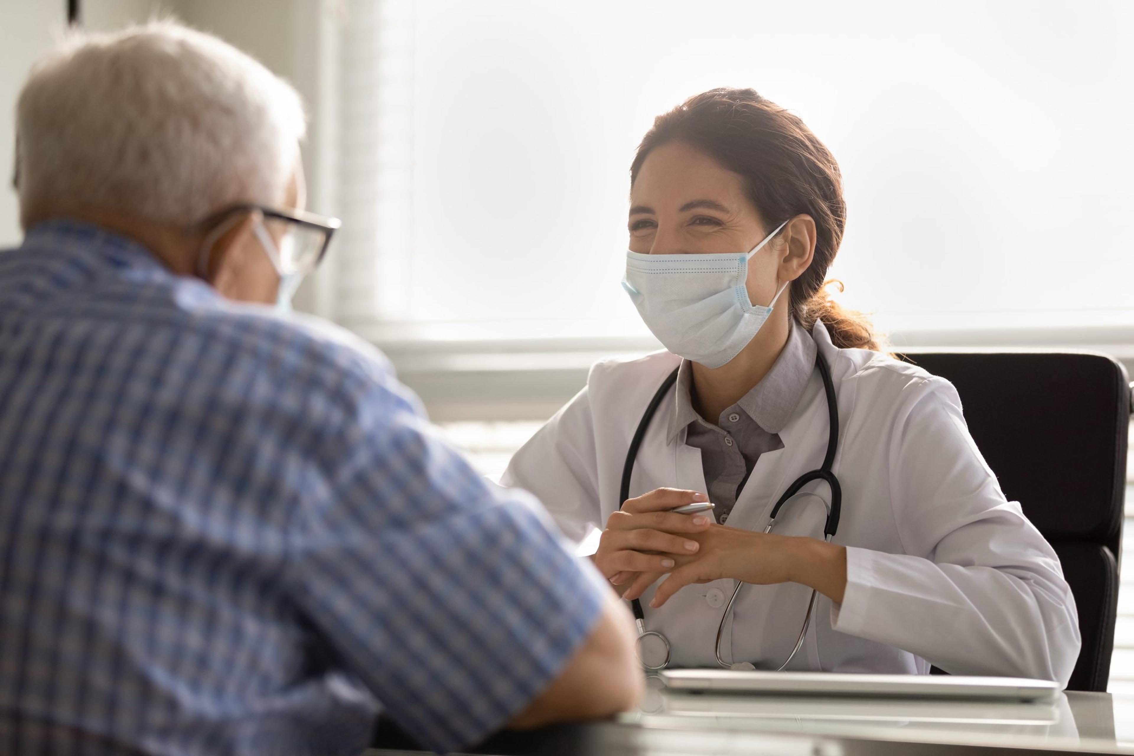 Smiling doctor in facemask consult senior male patient