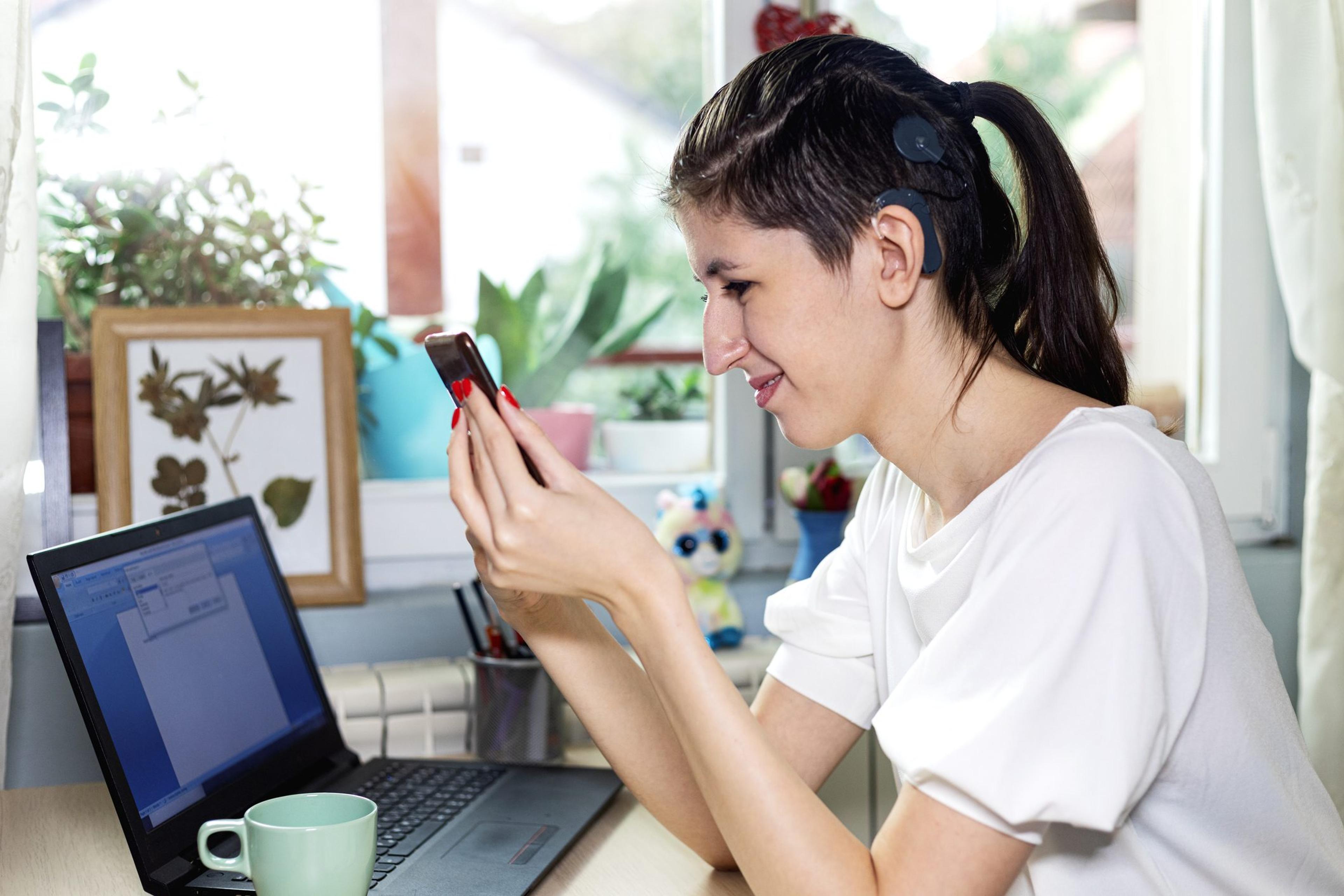 Woman with a cochlear implant checking her phone while working at her laptop