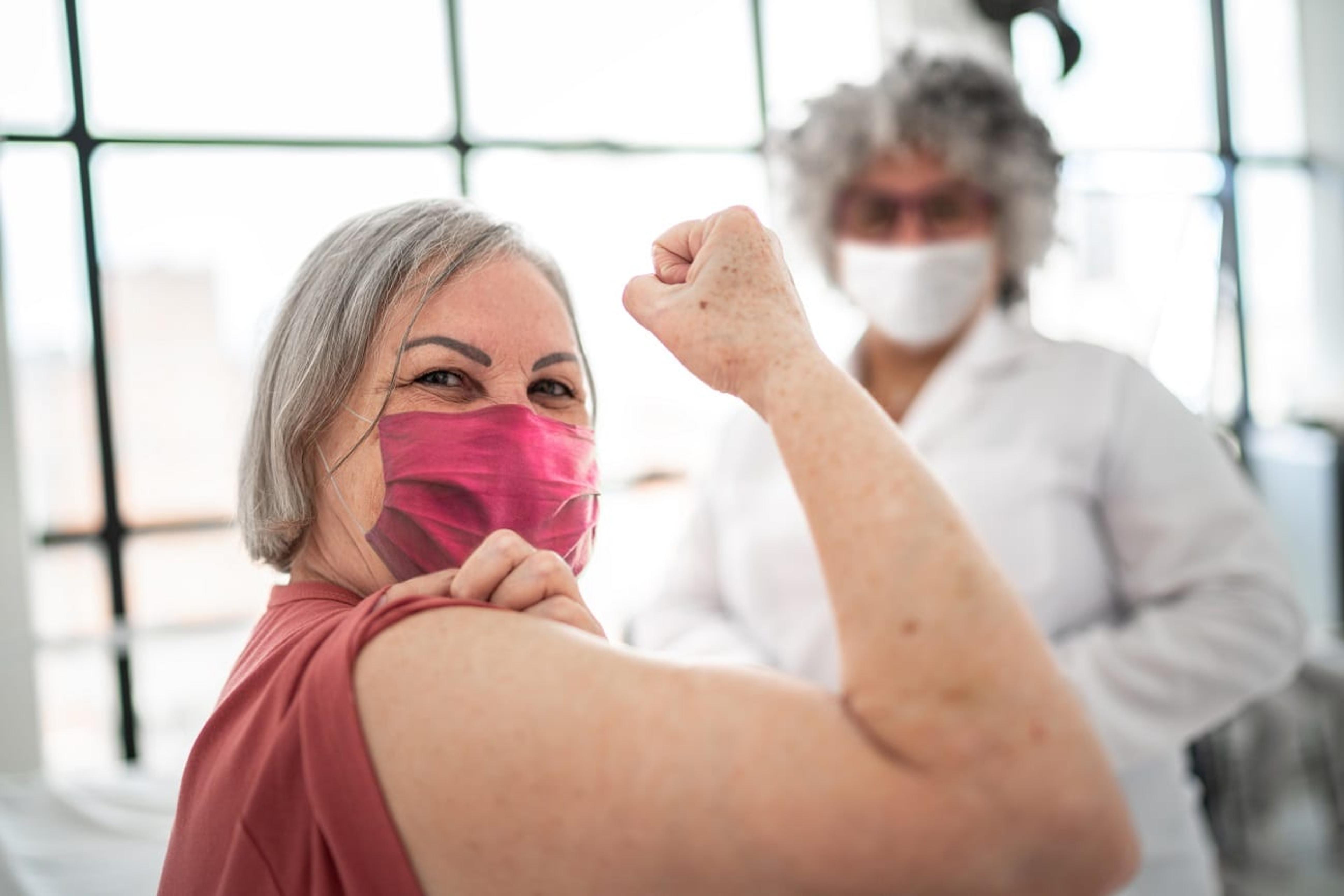 Woman wearing a mask curls her arm in a pose after being vaccinated