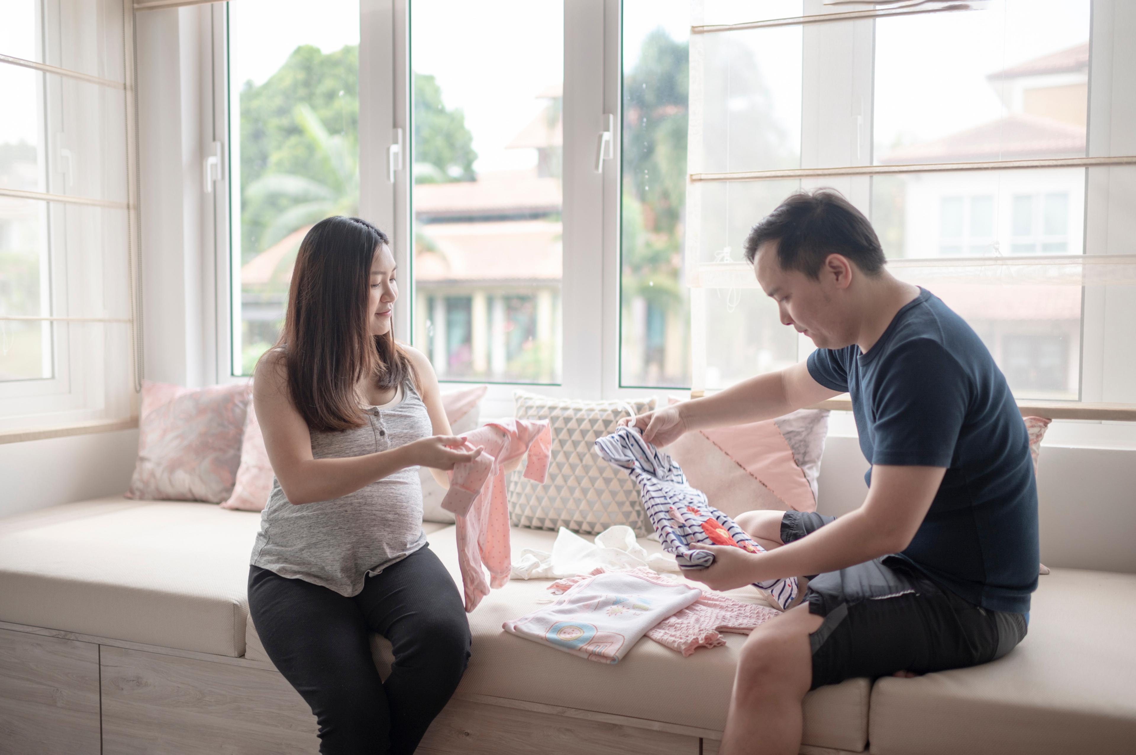 Pregnant woman sorts baby clothes with the father to be