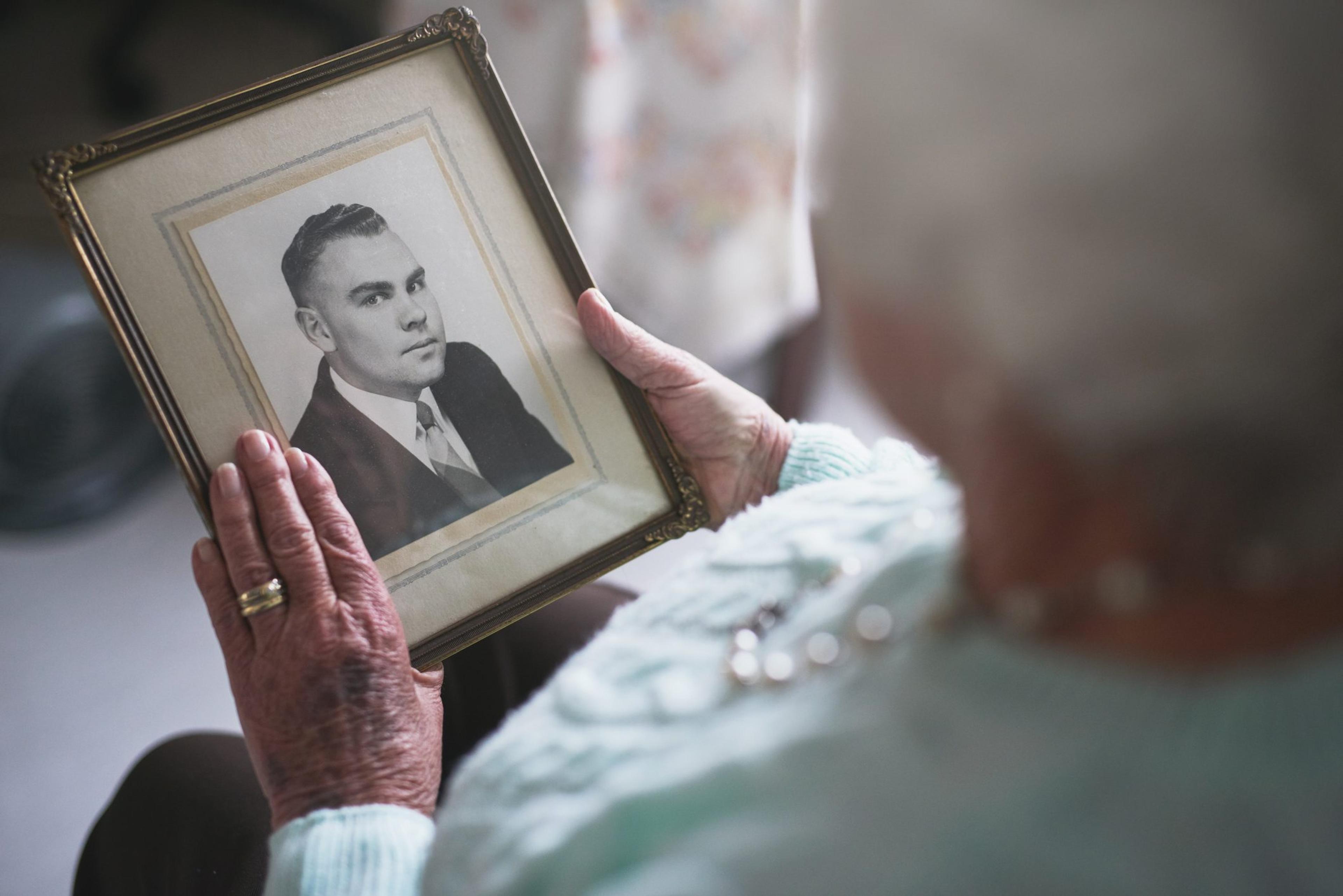 Older woman holds a framed picture of her husband as a young man
