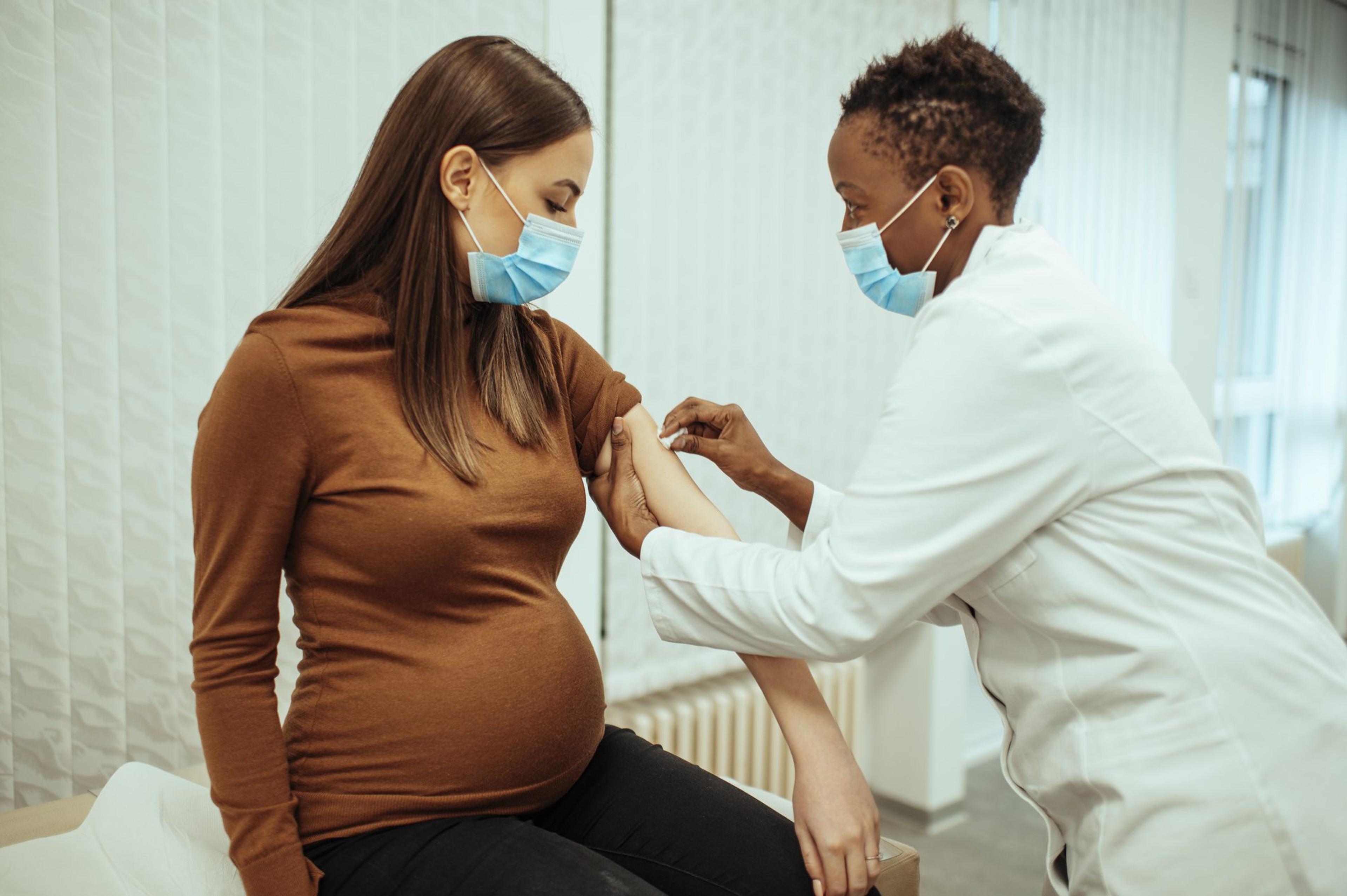 Pregnant woman wearing a mask receives a covid-19 vaccine from a female doctor wearing a mask
