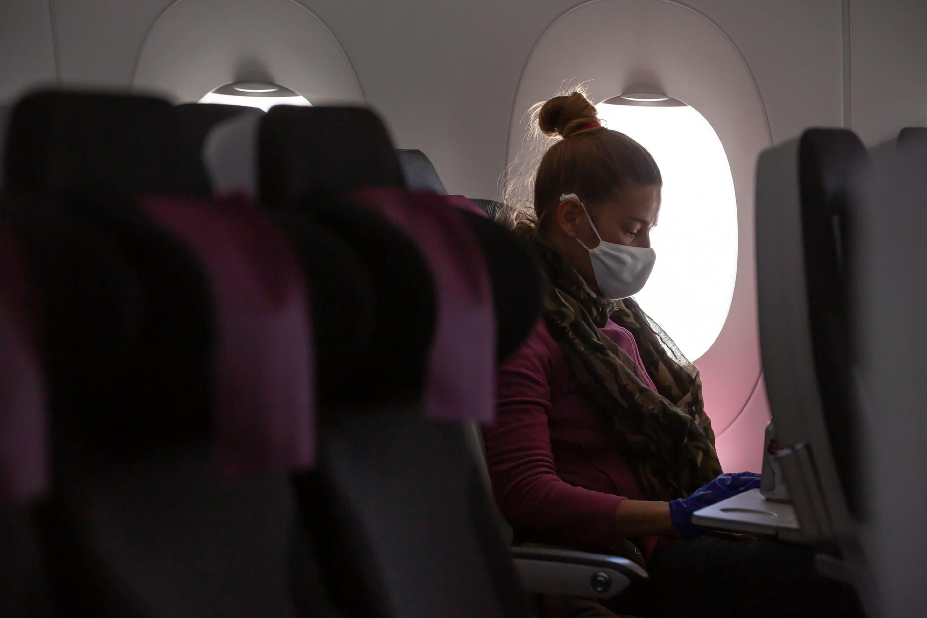 Woman wearing a mask sits on an airplane.