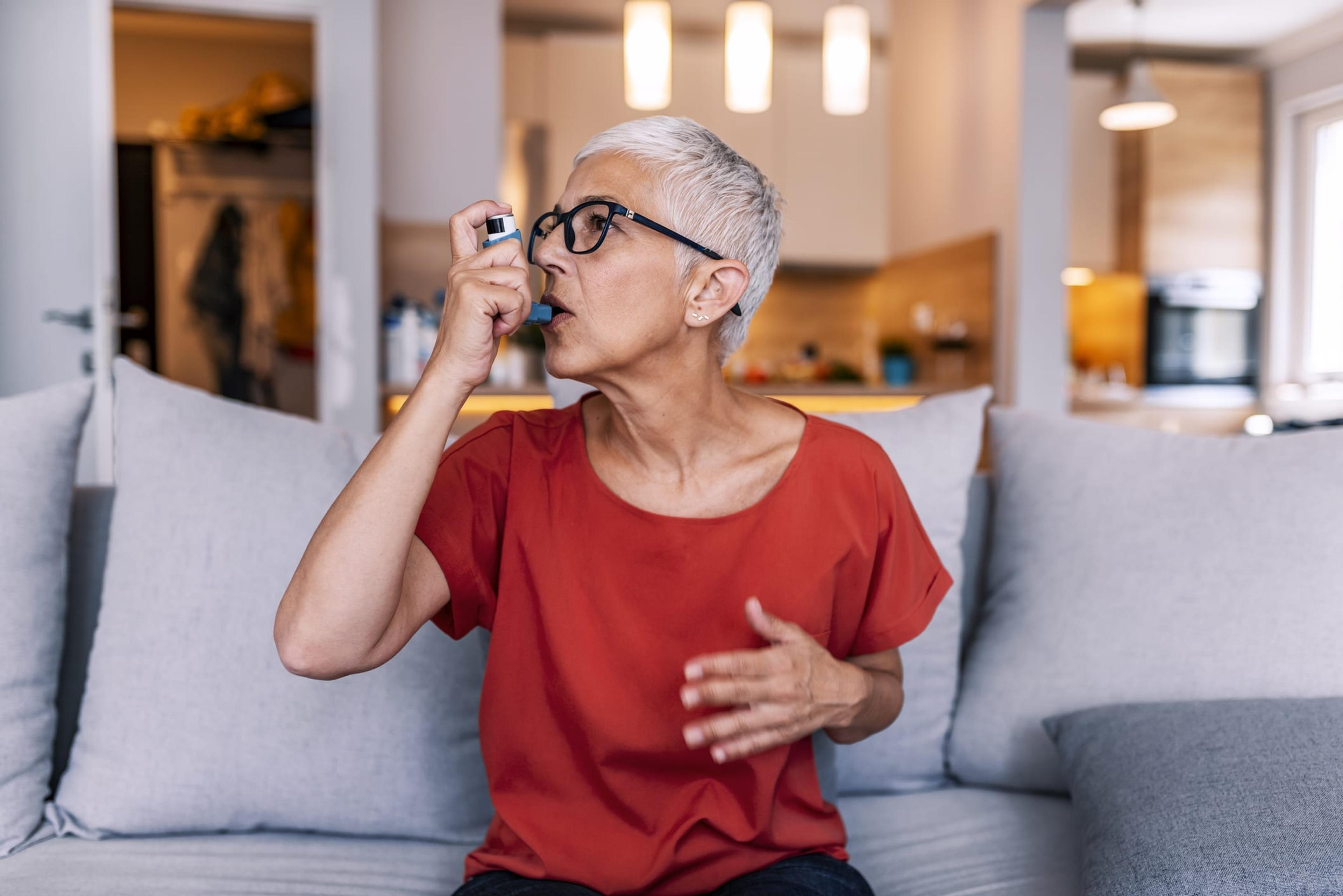 Woman taking an inhaler while sitting on the couch