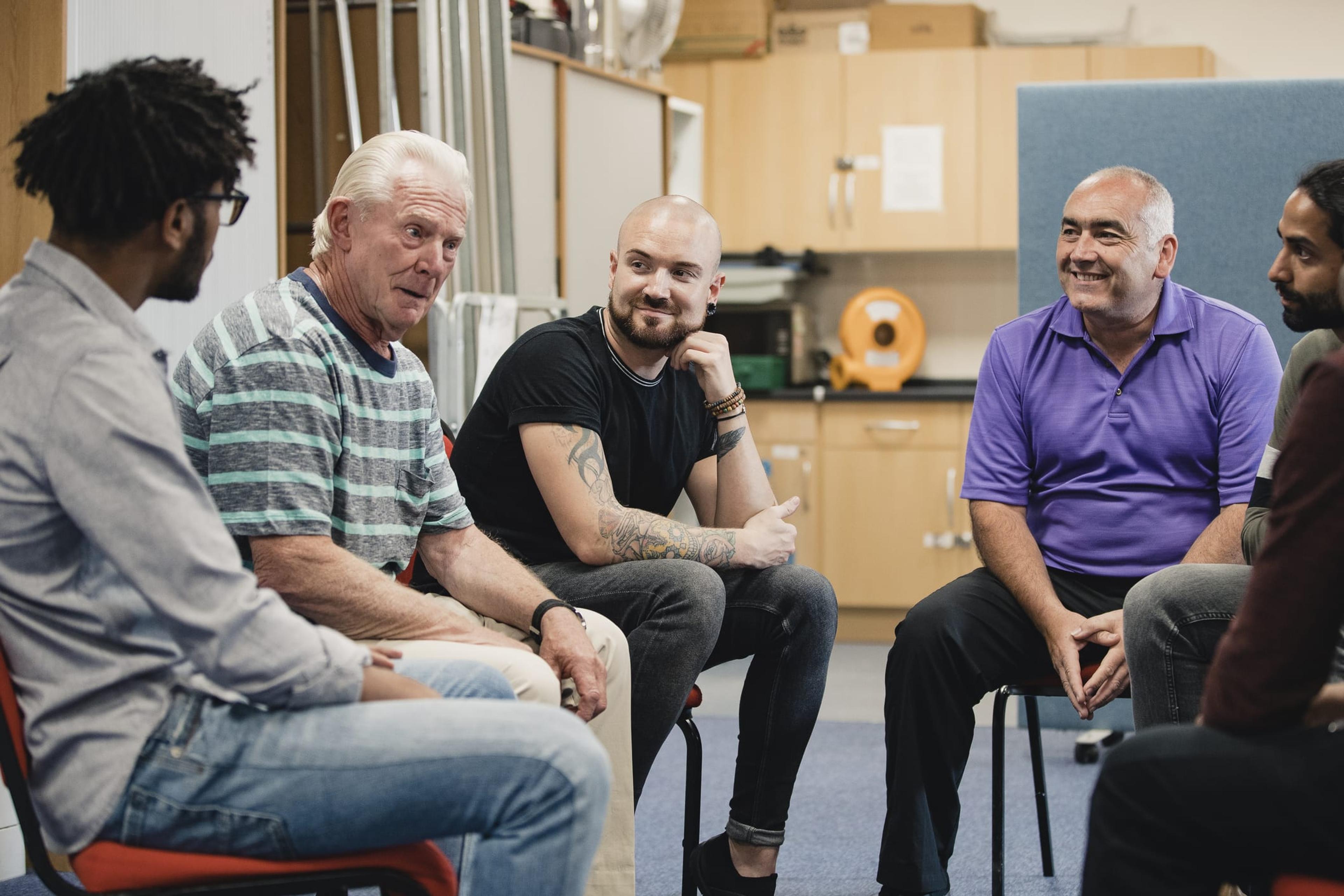 Group of diverse men sit in a circle talking and smiling