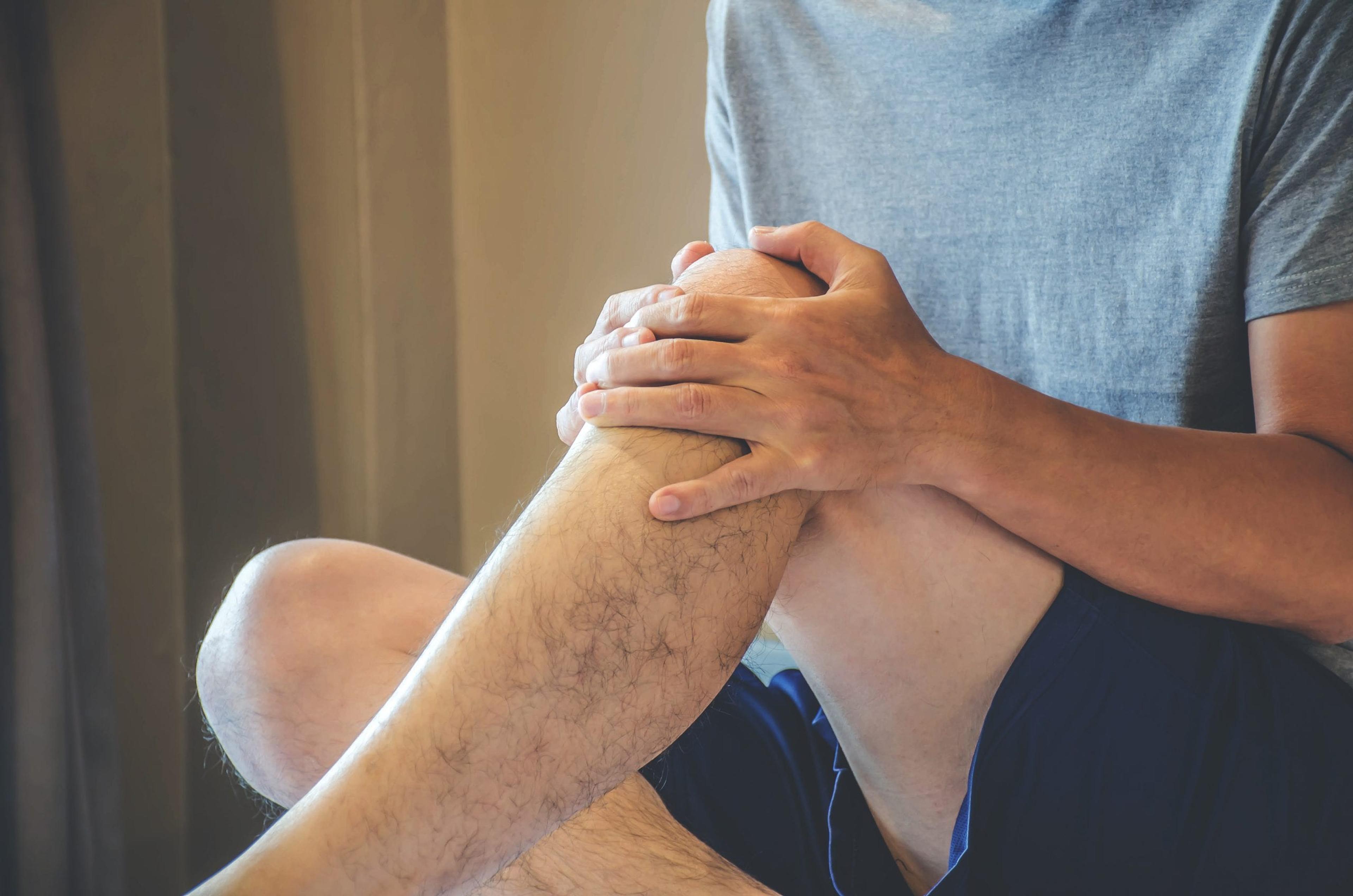 Man sitting cross-legged on bed holding his knee.