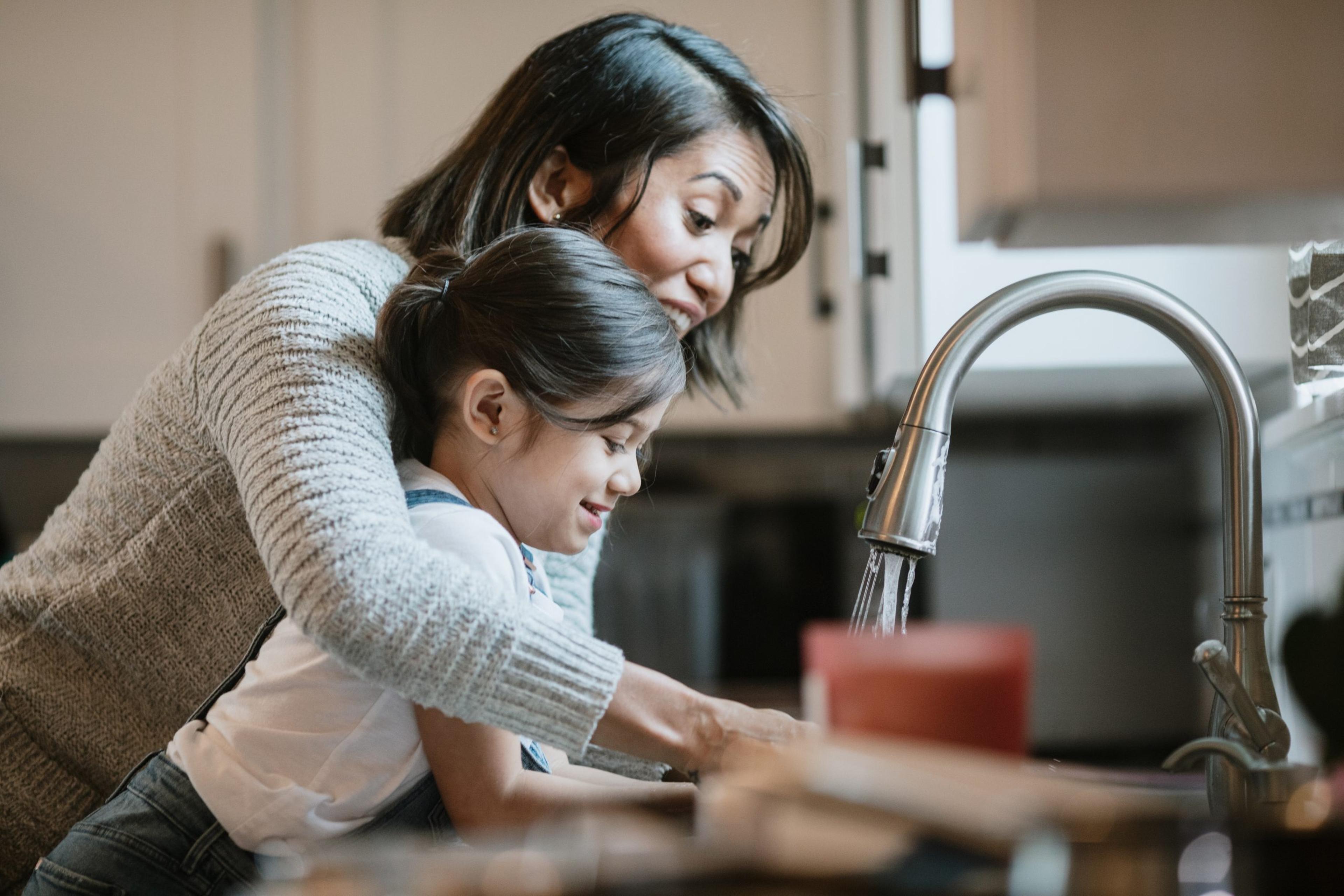 Mom helping her daughter wash hands