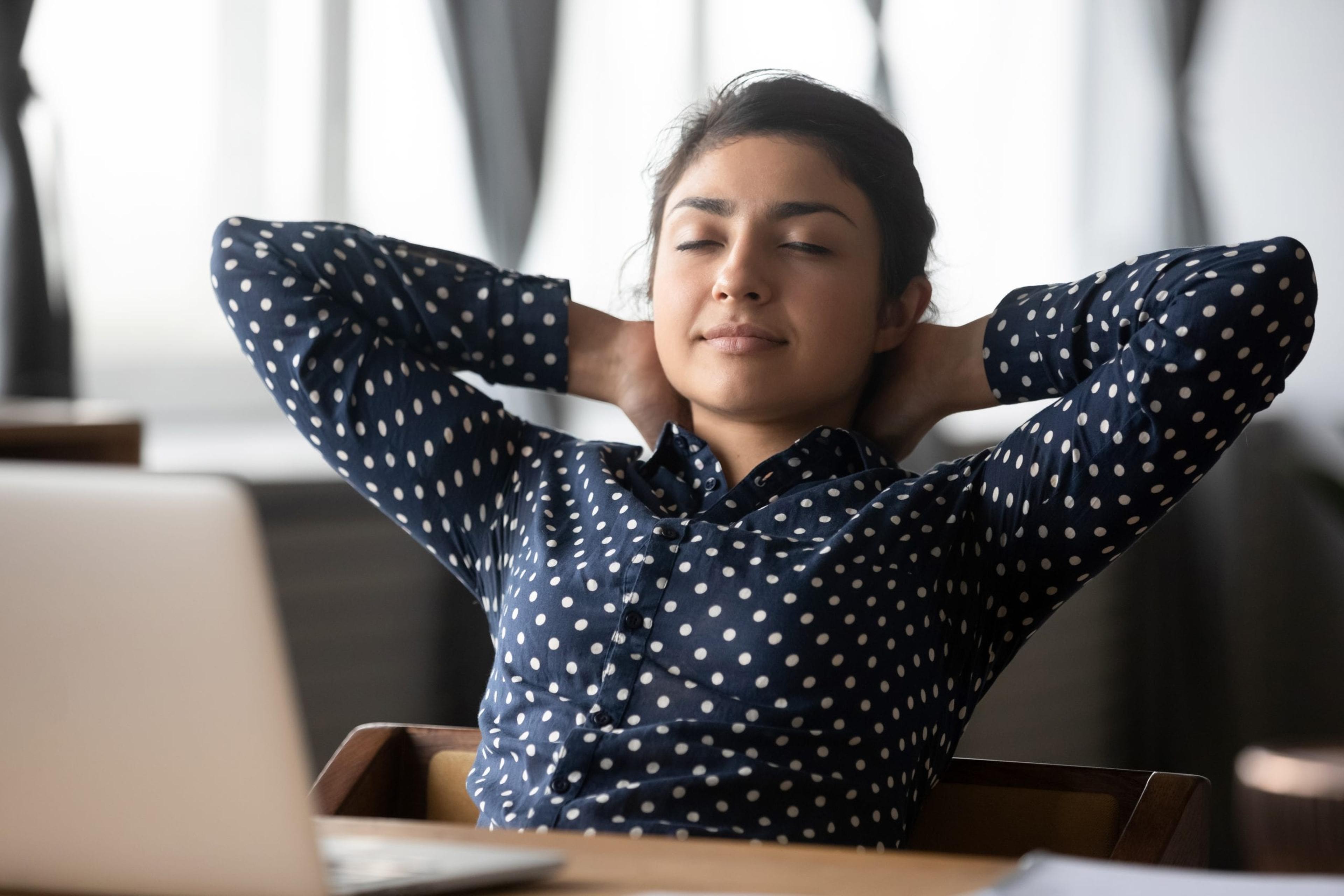 Calm tired ethnic young woman sit lean back in chair at workplace relax with eyes closed take nap, exhausted millennial Indian girl rest at desk daydreaming or sleeping at home, fatigue concept