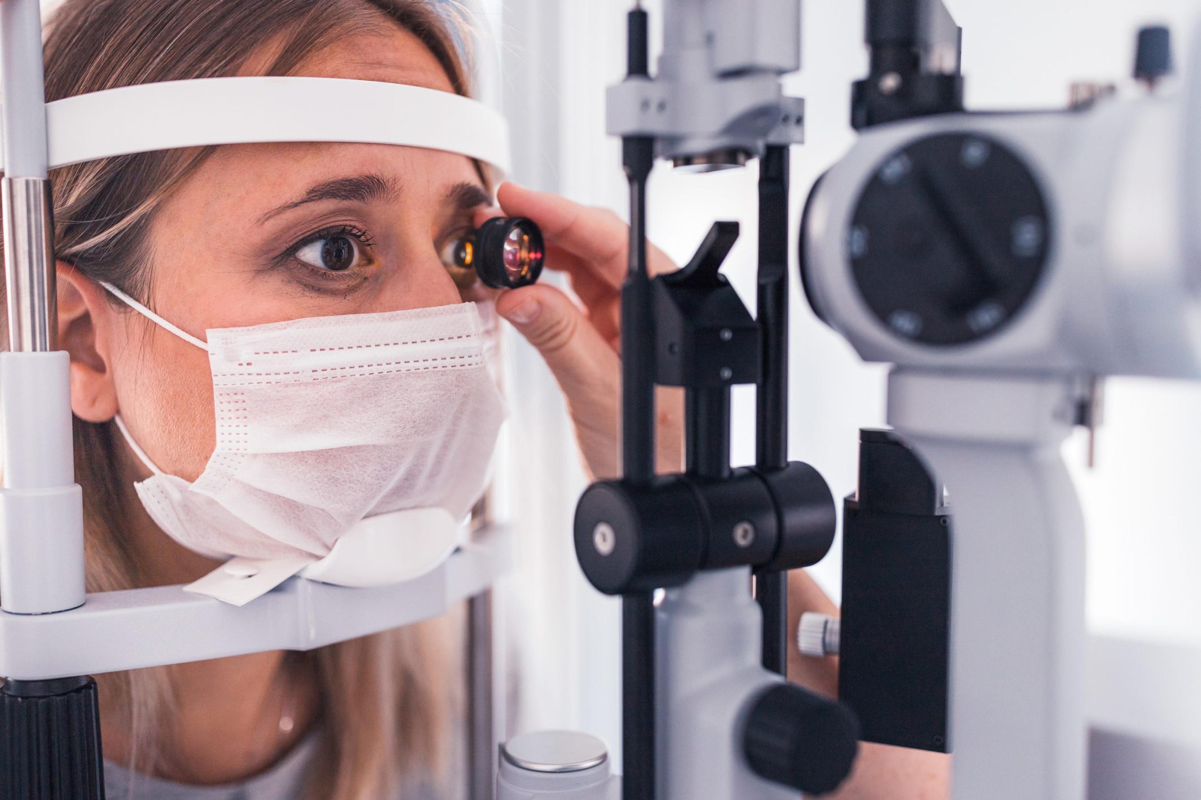 A young woman with long, sandy hair peers through a lense in an eye exam.