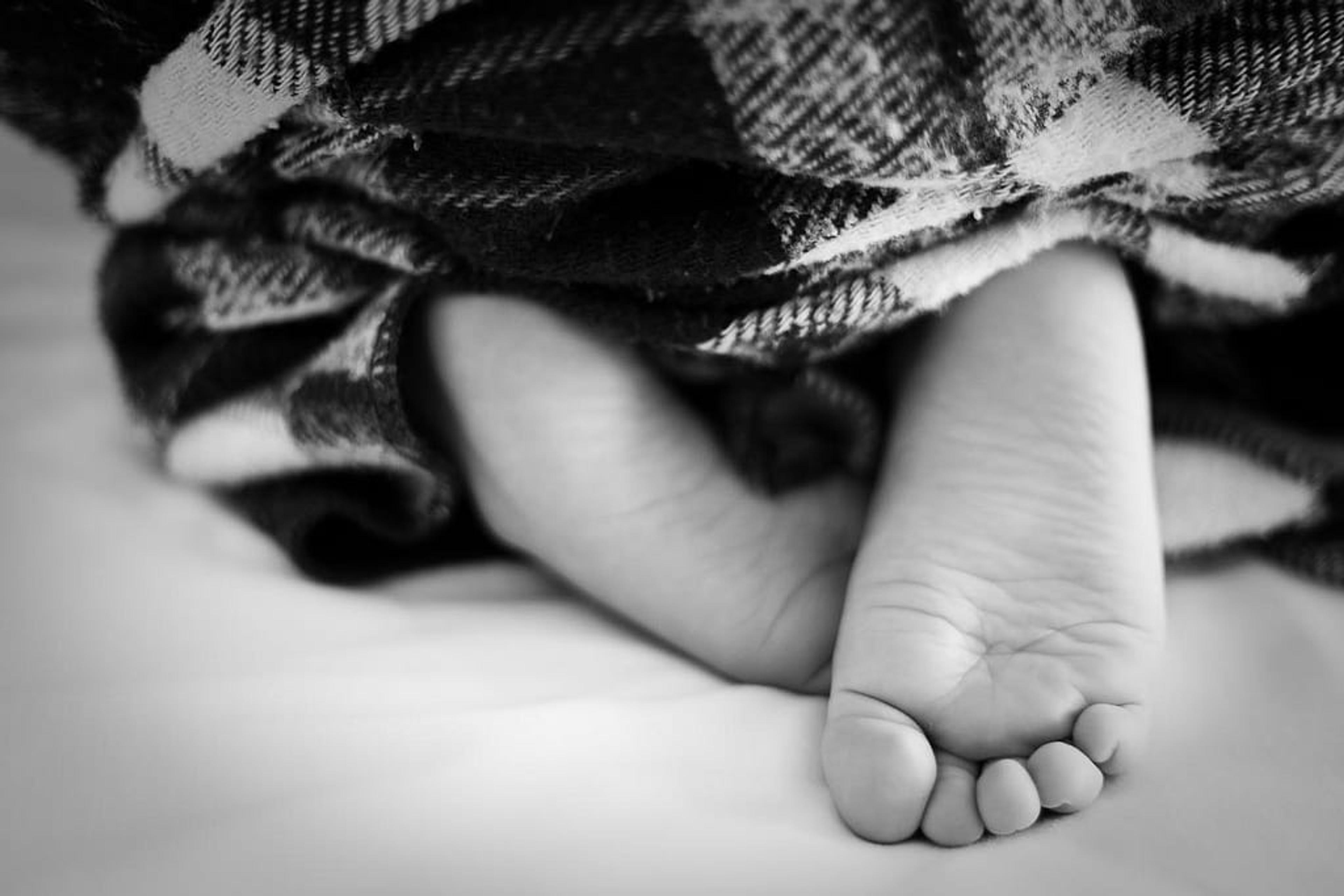 Black and white image of a child's feet under a blanket