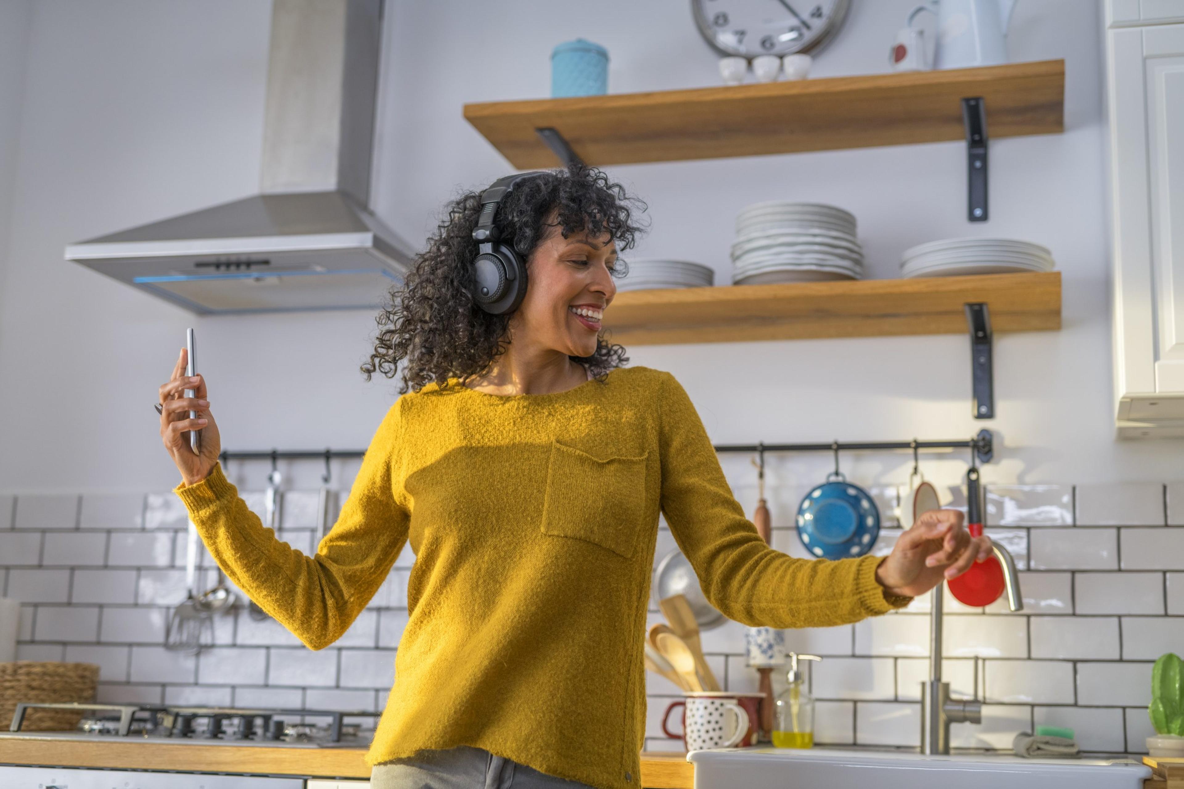 Mid adult woman dancing in kitchen while listening music