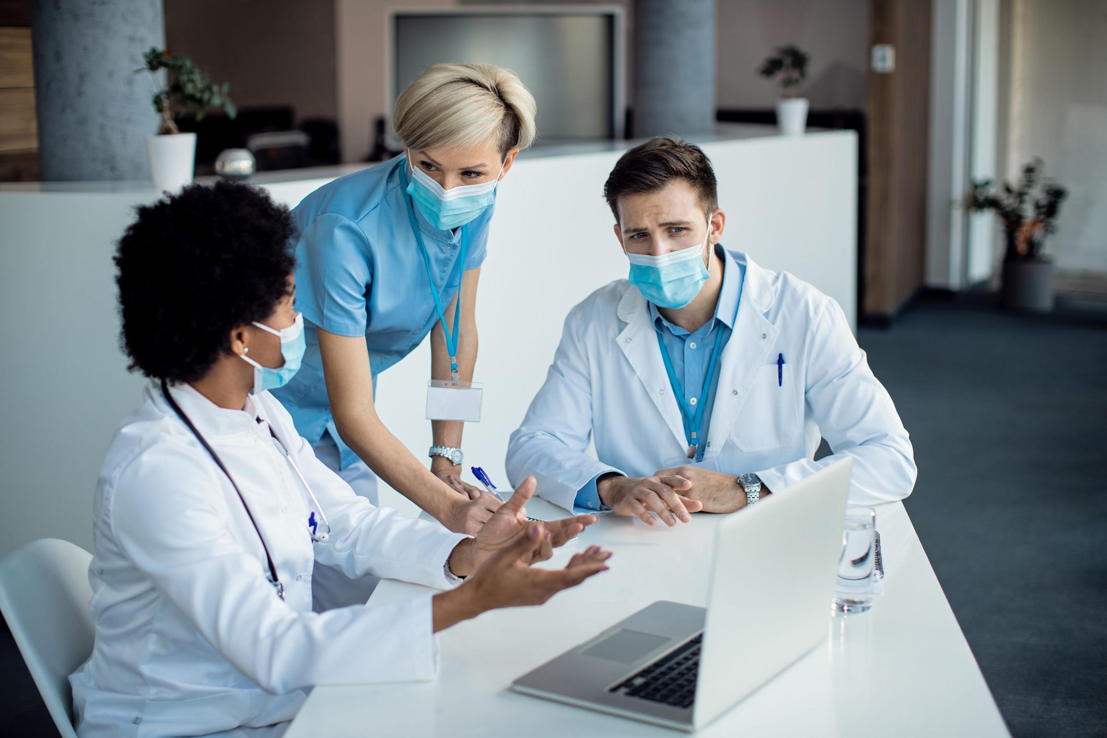 Group of health care workers wearing masks gathered around a laptop discussing data