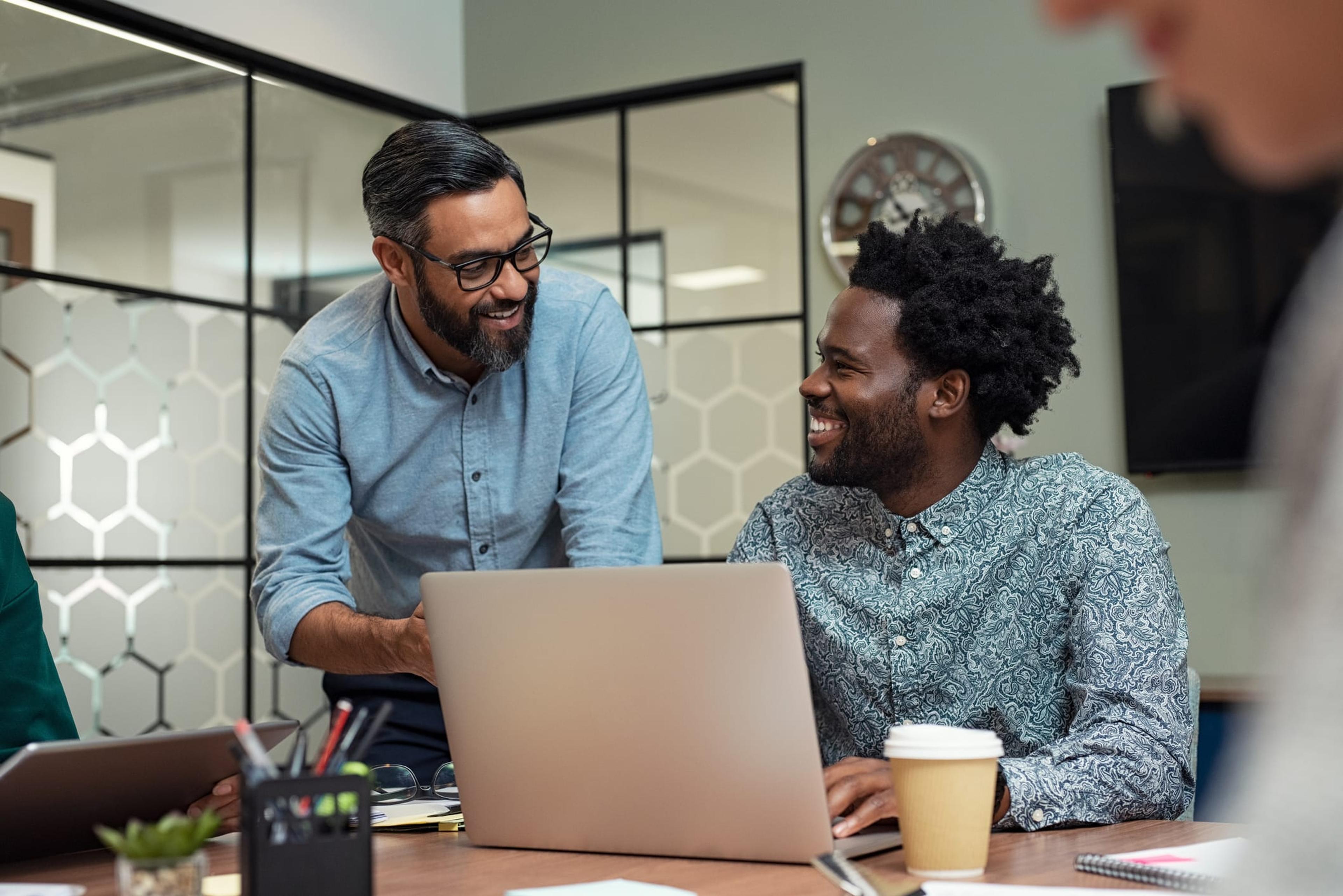 Two men smile in the office as they look at a laptop