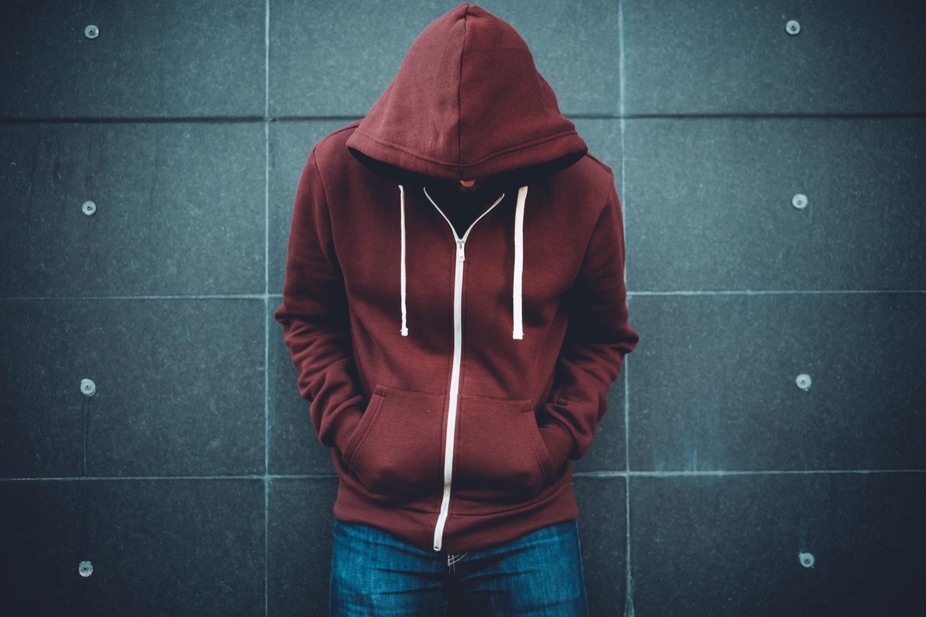 Man with head down, wearing hoodie, leaning against a wall.
