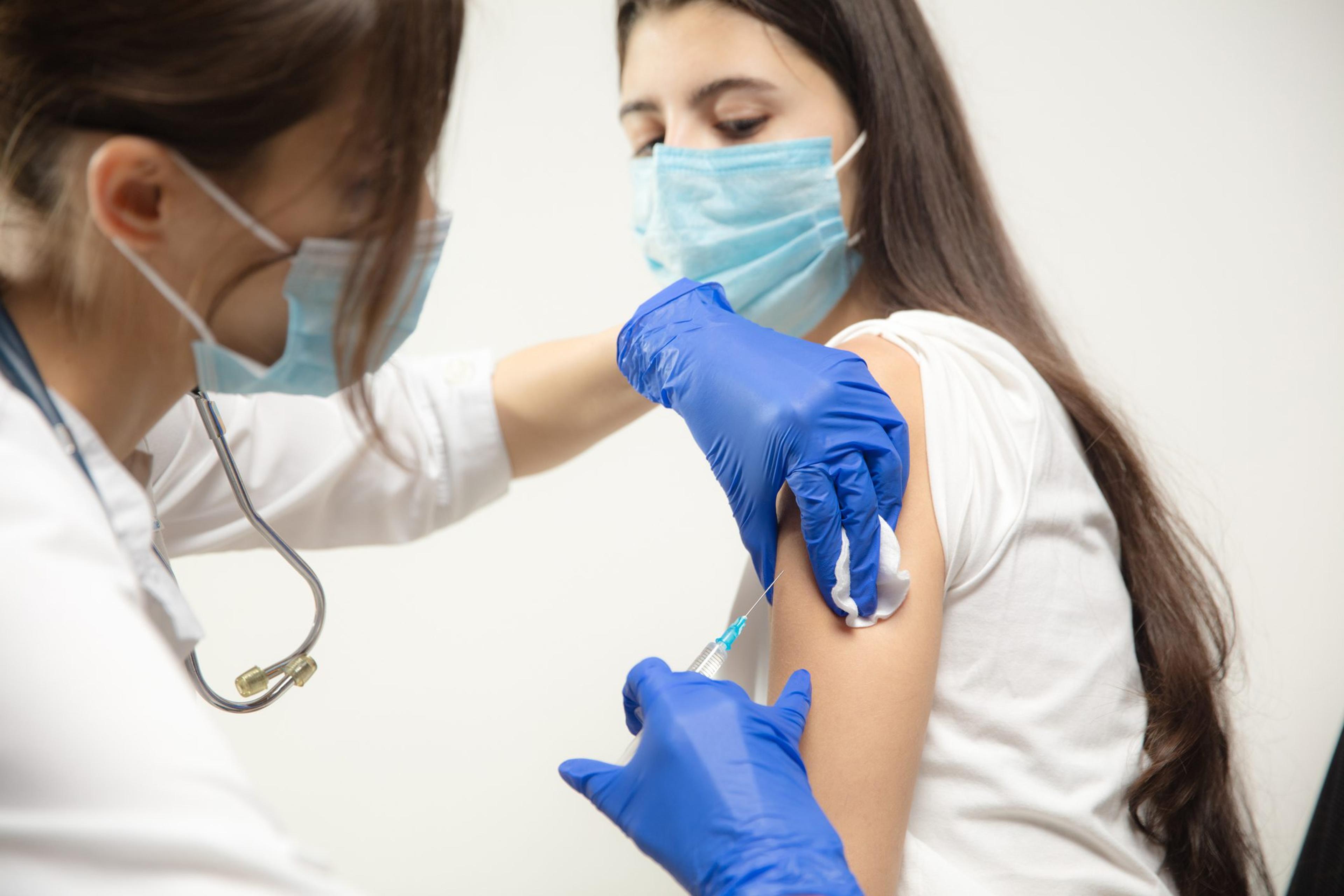 Nurse wearing mask and gloves administers a COVID vaccine to a patient wearing a mask