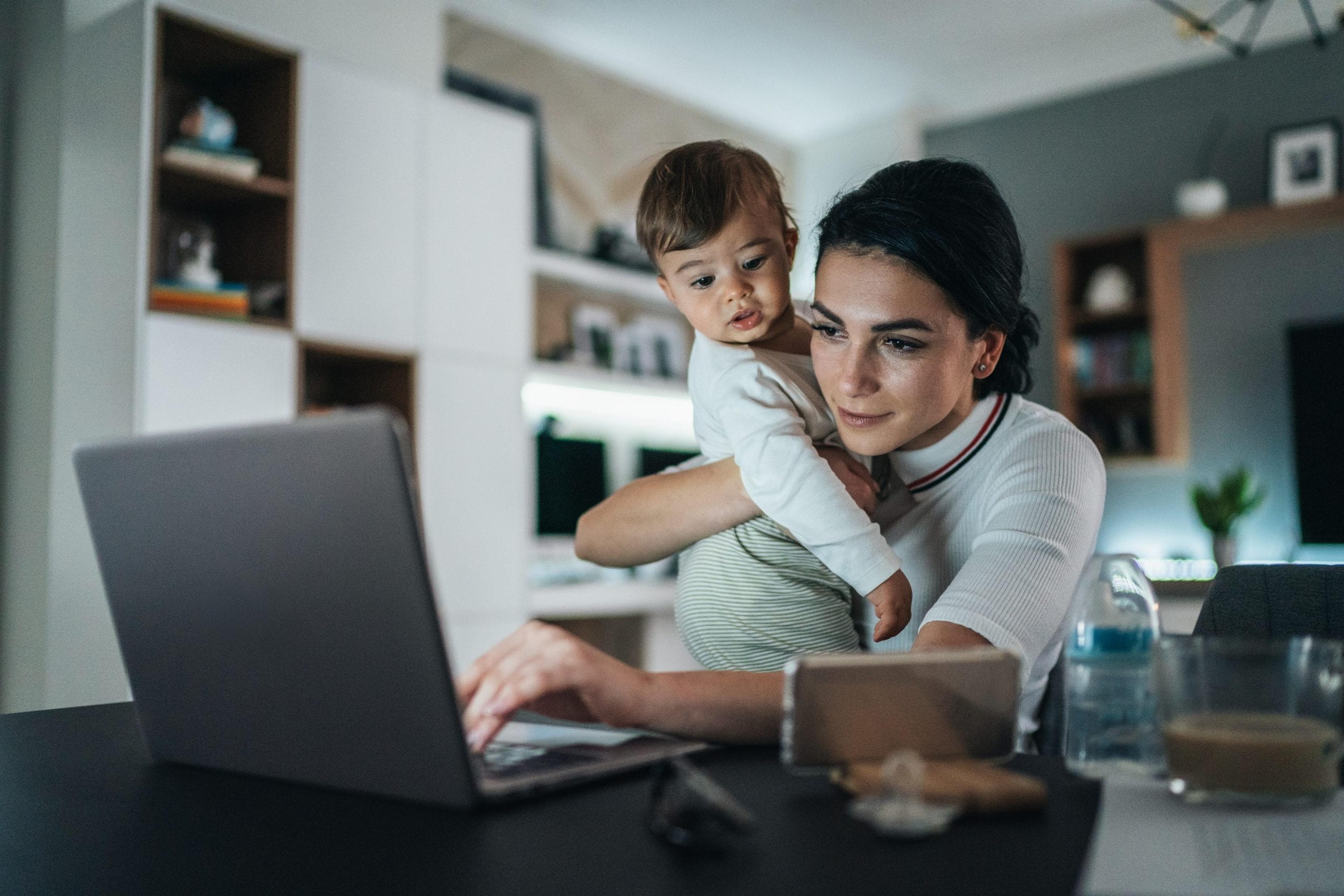 Young mom working on laptop holding a baby