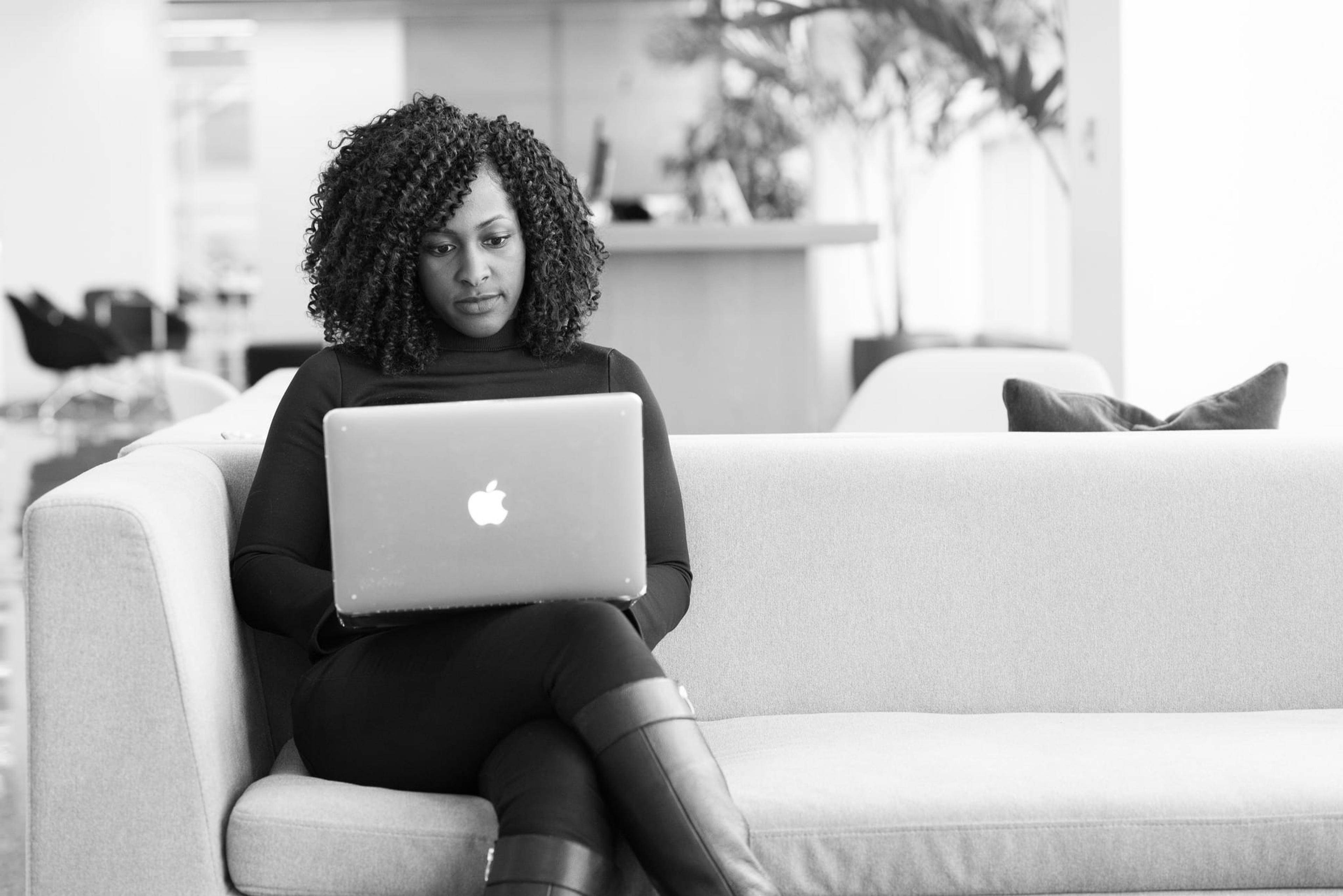 black and white photo of a woman sitting on a couch with a laptop.