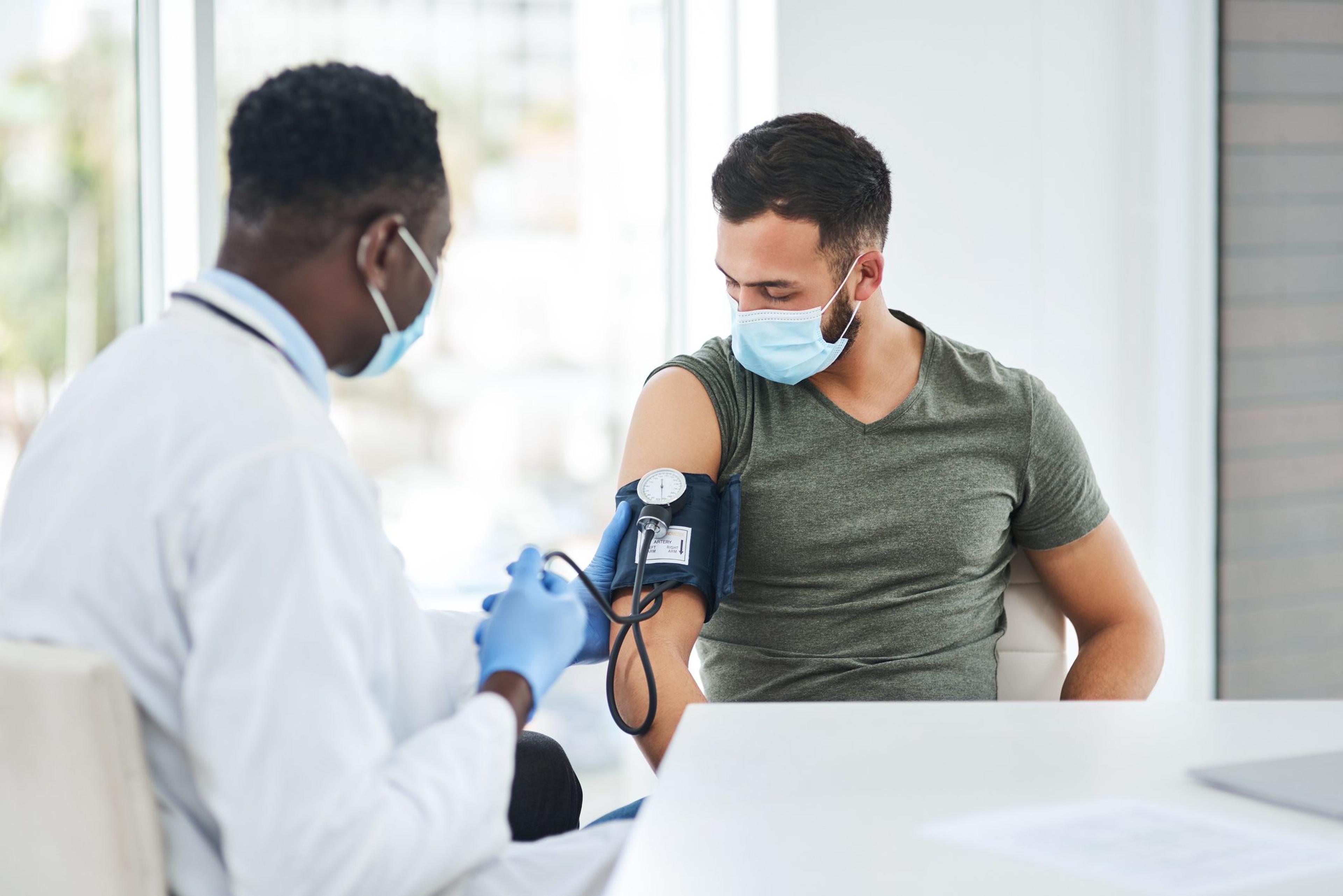 Doctor wearing a mask checks the blood pressure of a young man wearing a mask