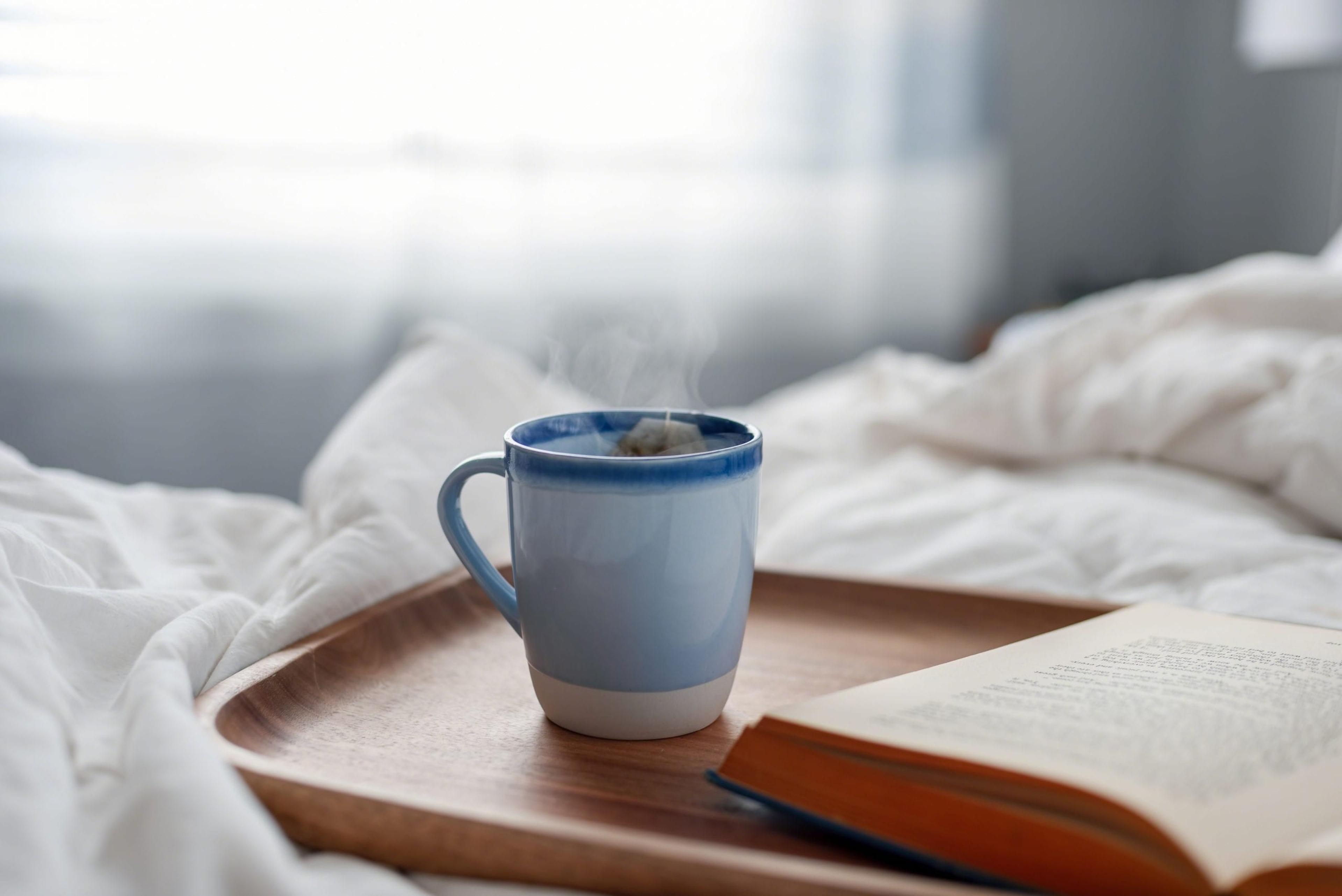 Tray with book and cup of hot tea in bed