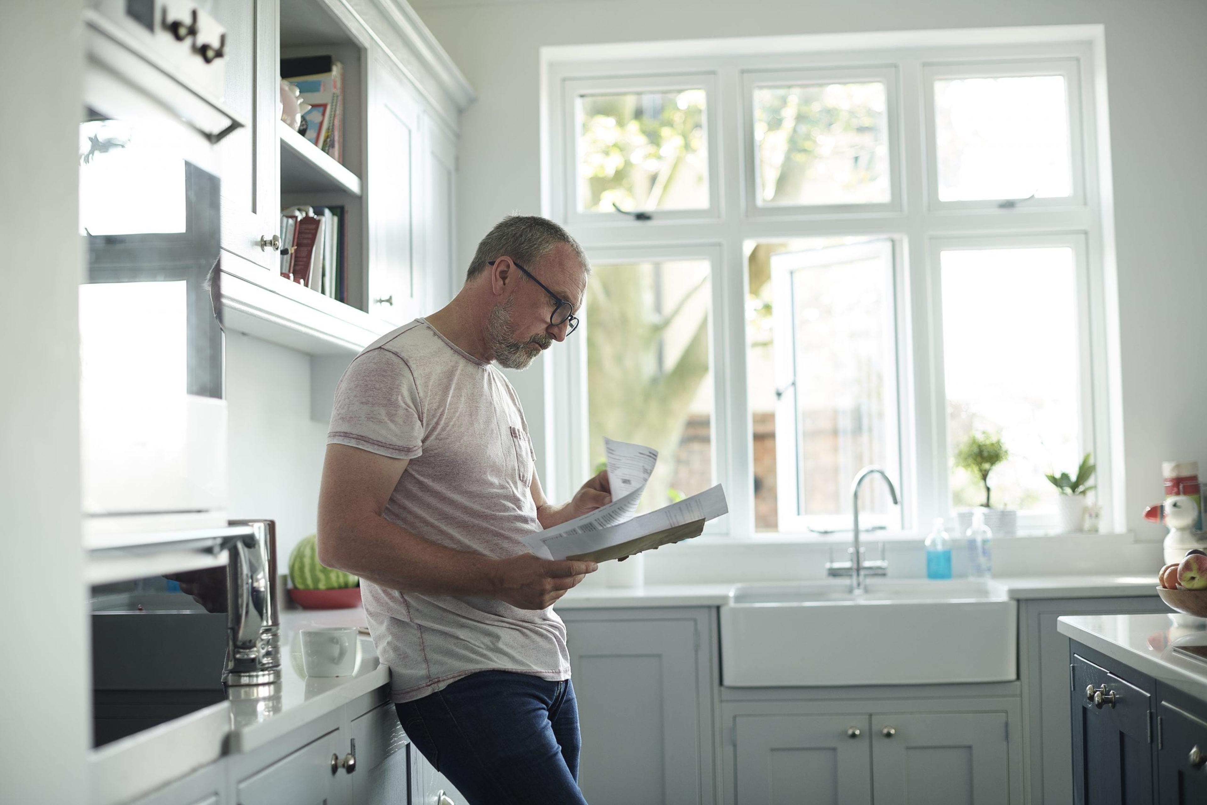 Man stands in a kitchen looking at paperwork.